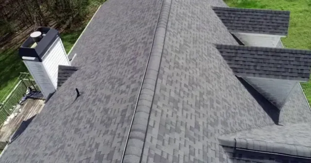Aerial view of a gray shingled roof with vents and a chimney