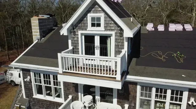Aerial view of a house with gray roof, white trim, dormer windows, and a small balcony.