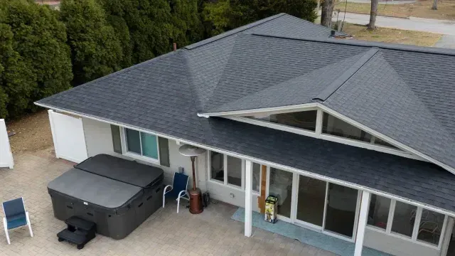 Aerial view of a house with a gray roof, white exterior, and a covered patio with a hot tub.
