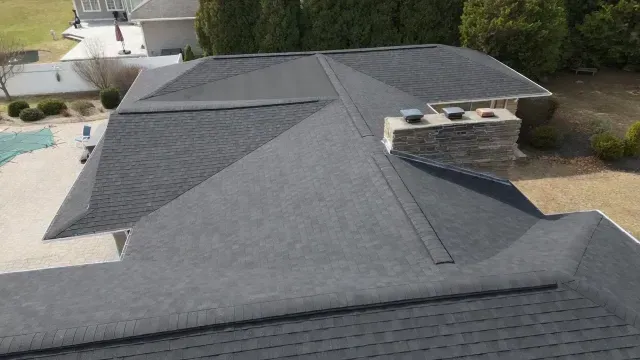 Aerial view of a dark gray shingled roof with rooftop vents and a small stone chimney.