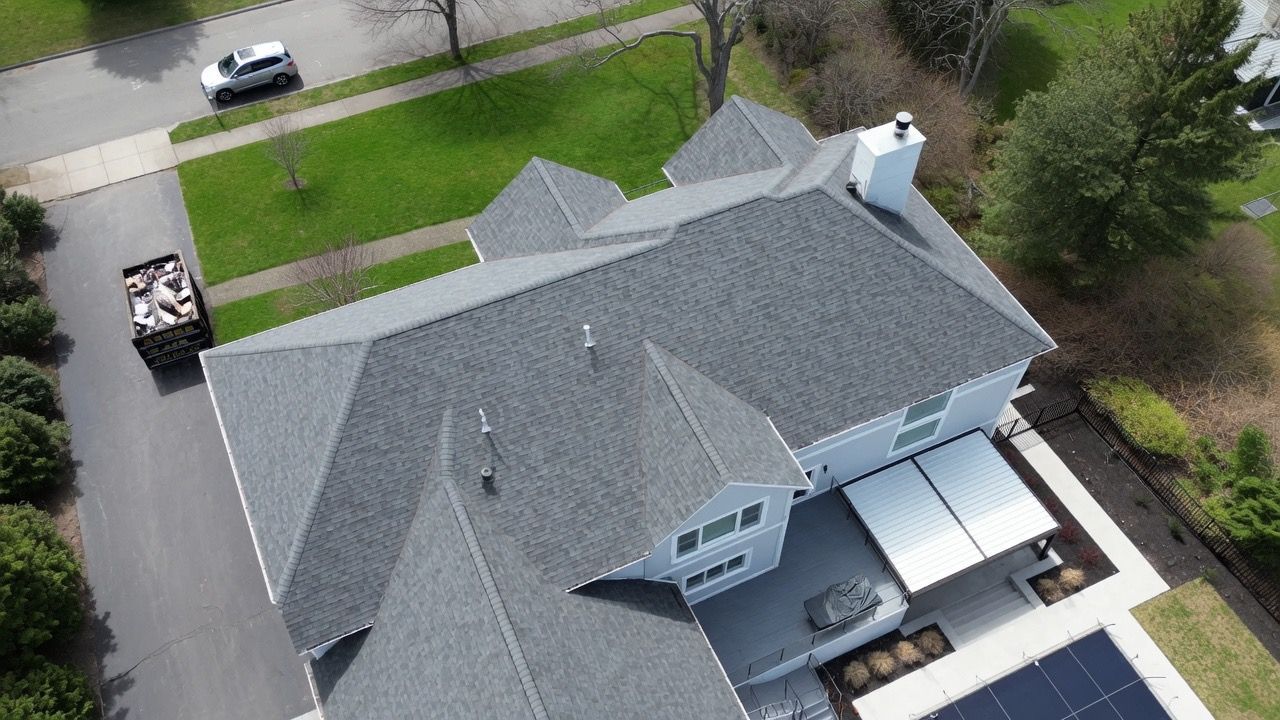Aerial view of a gray-roofed suburban house with driveway, lawn, and parked vehicles