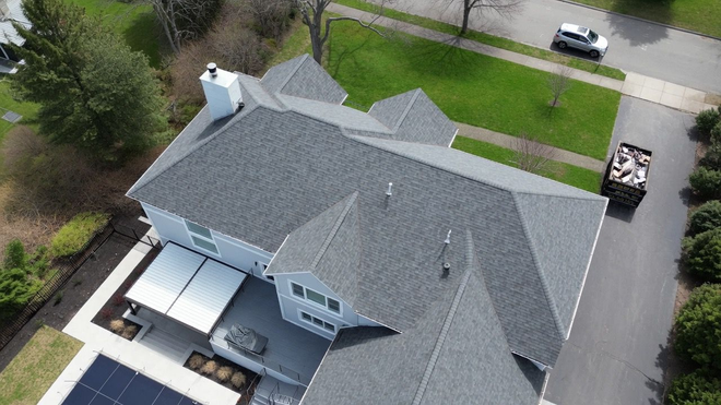 Aerial view of a gray-roofed suburban house with driveway, garage, and surrounding lawn.