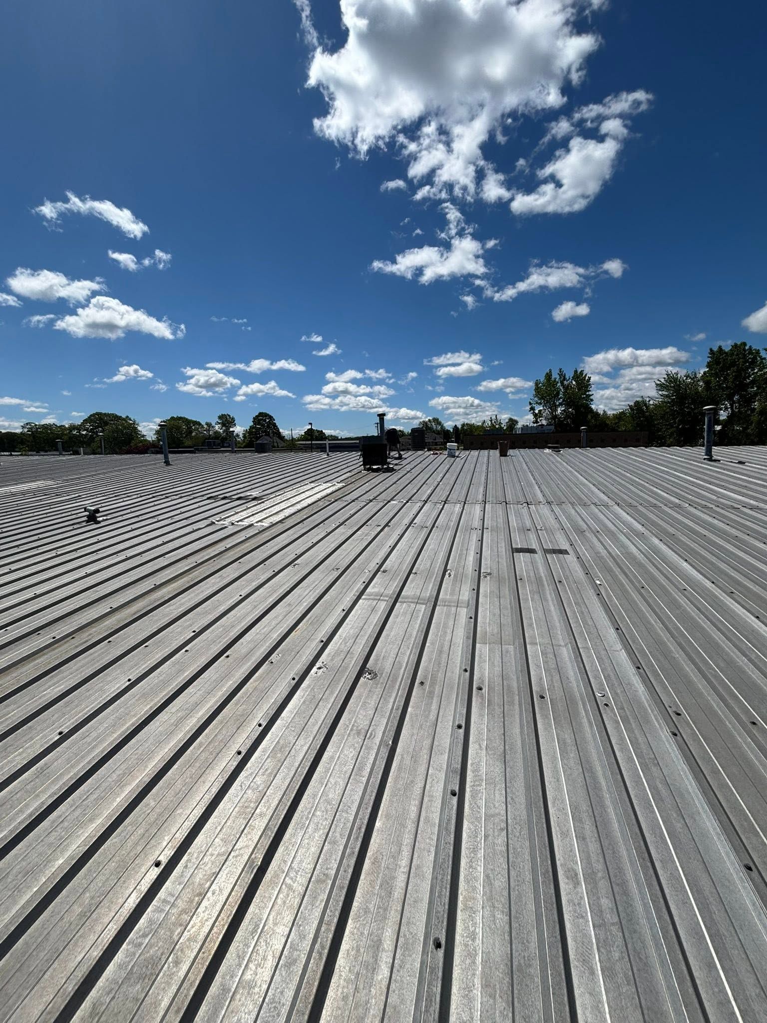 Rows of silver metal roofing under a bright blue sky with scattered clouds, viewed from a low angle.