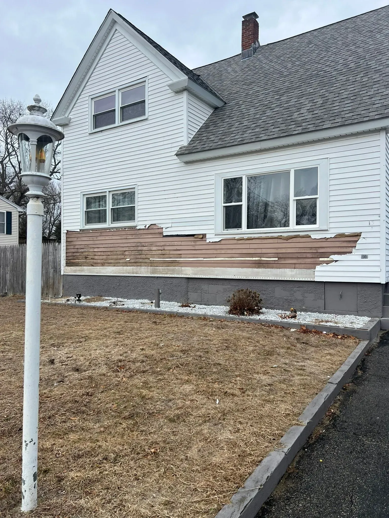 White house with damaged siding and a rock-covered front yard in winter.