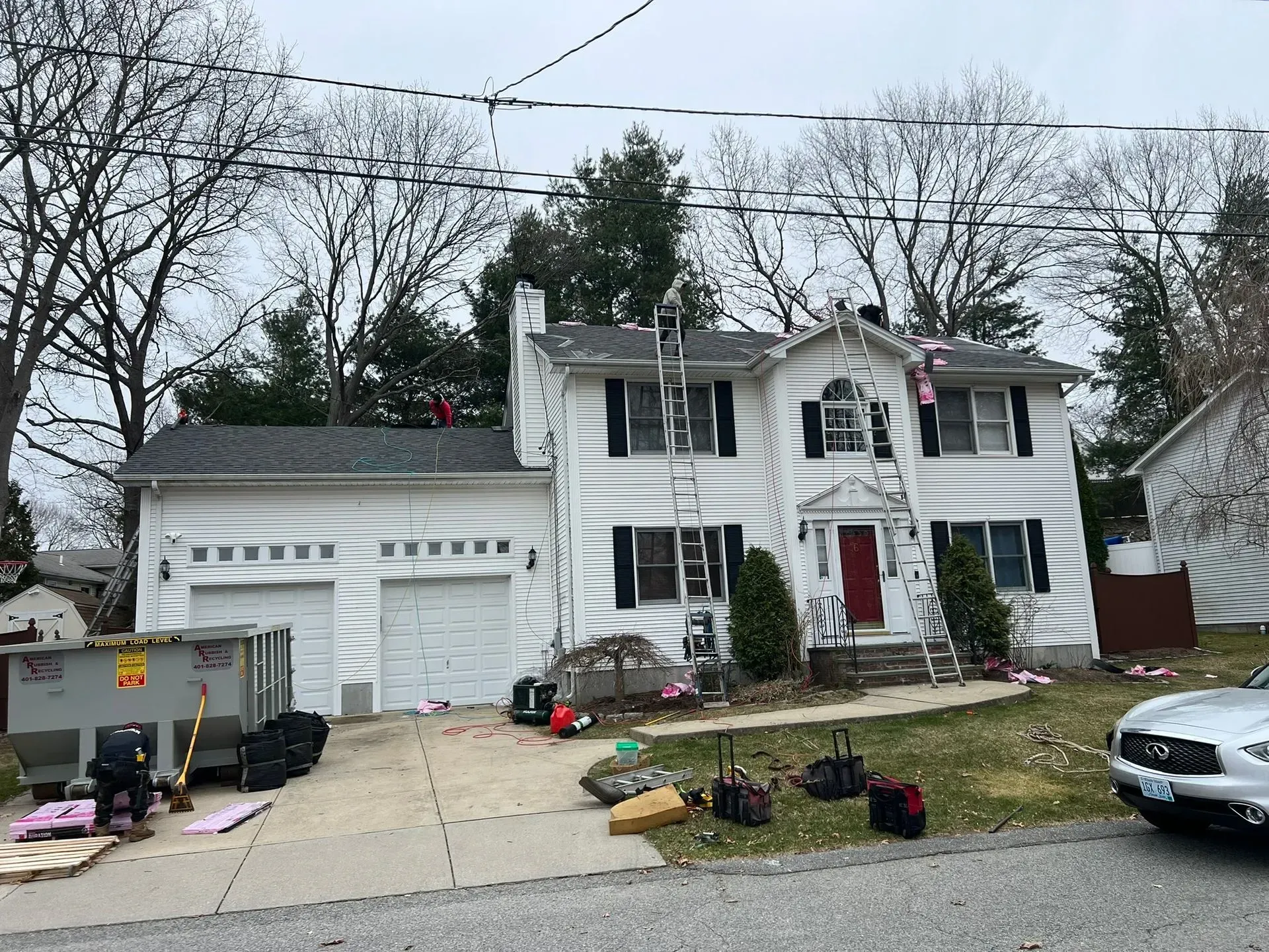 Two-story white house with garage, red front door, and ladders on the roof, decorated for the holidays