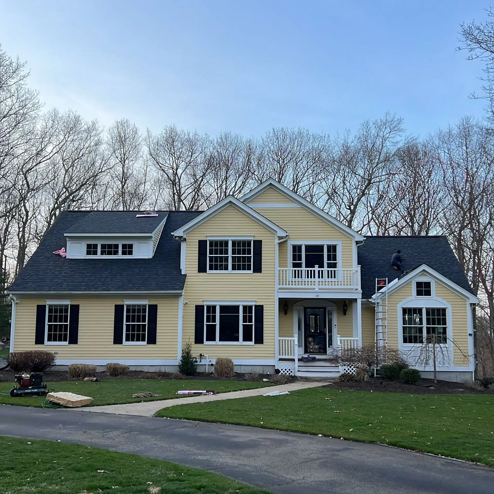 Large yellow and gray two-story house with a front porch, balcony, and curved driveway