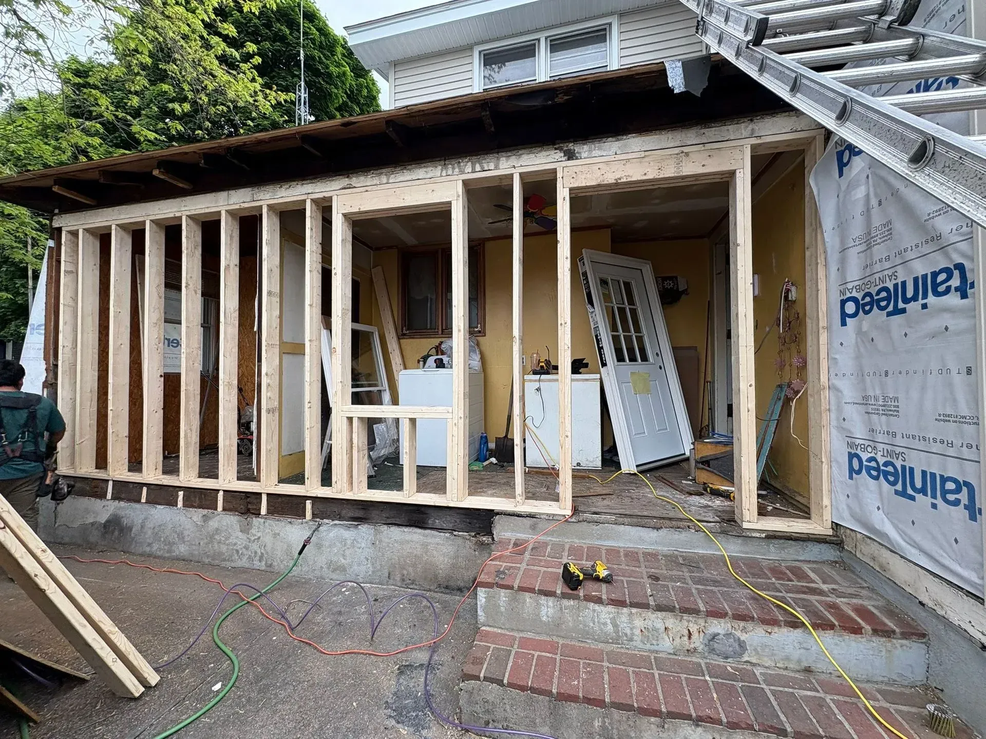 Partially framed house exterior under renovation with exposed wooden studs and construction materials