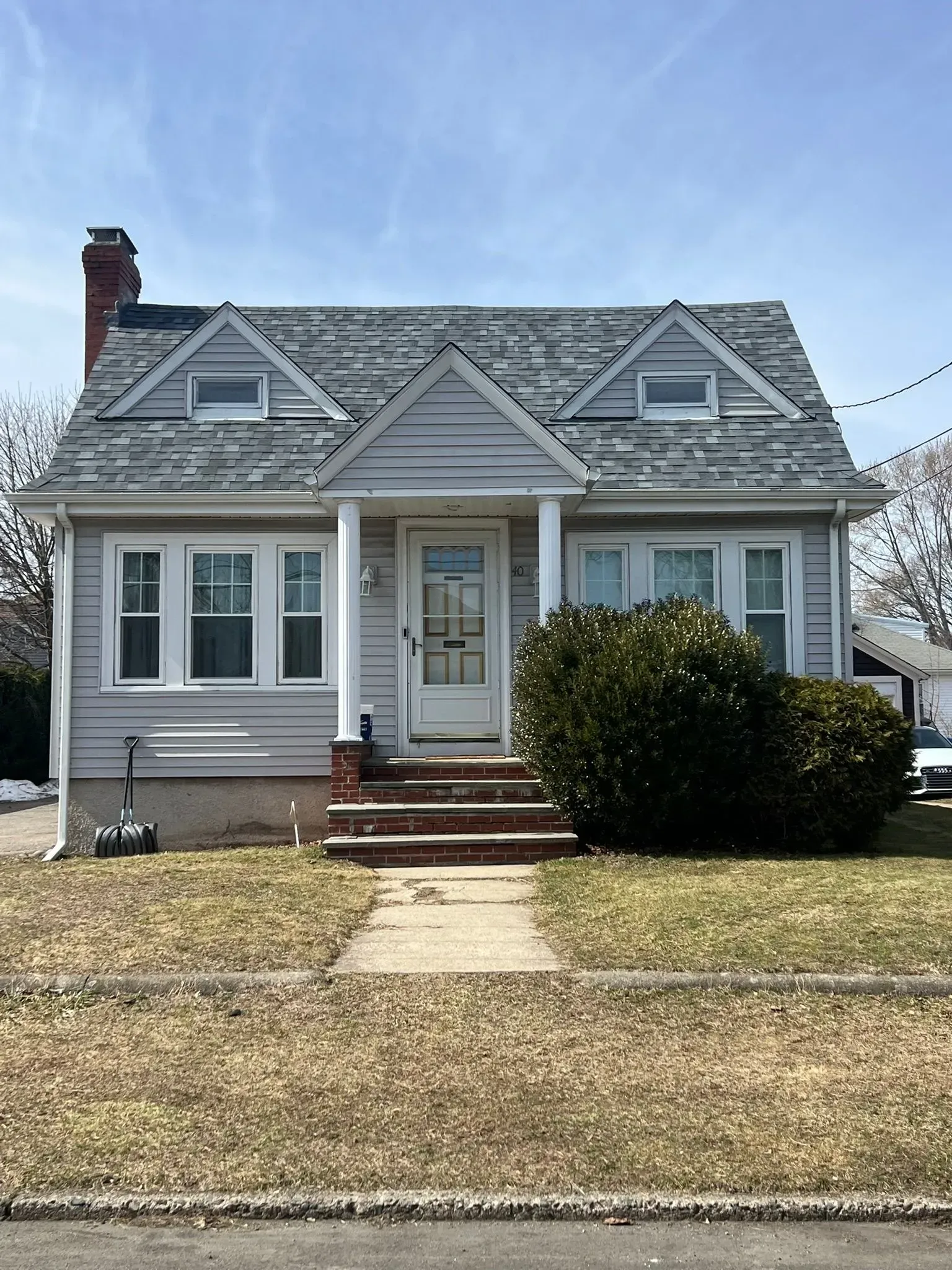 Small gray house with a steep roof, front porch, and brick steps in a suburban yard