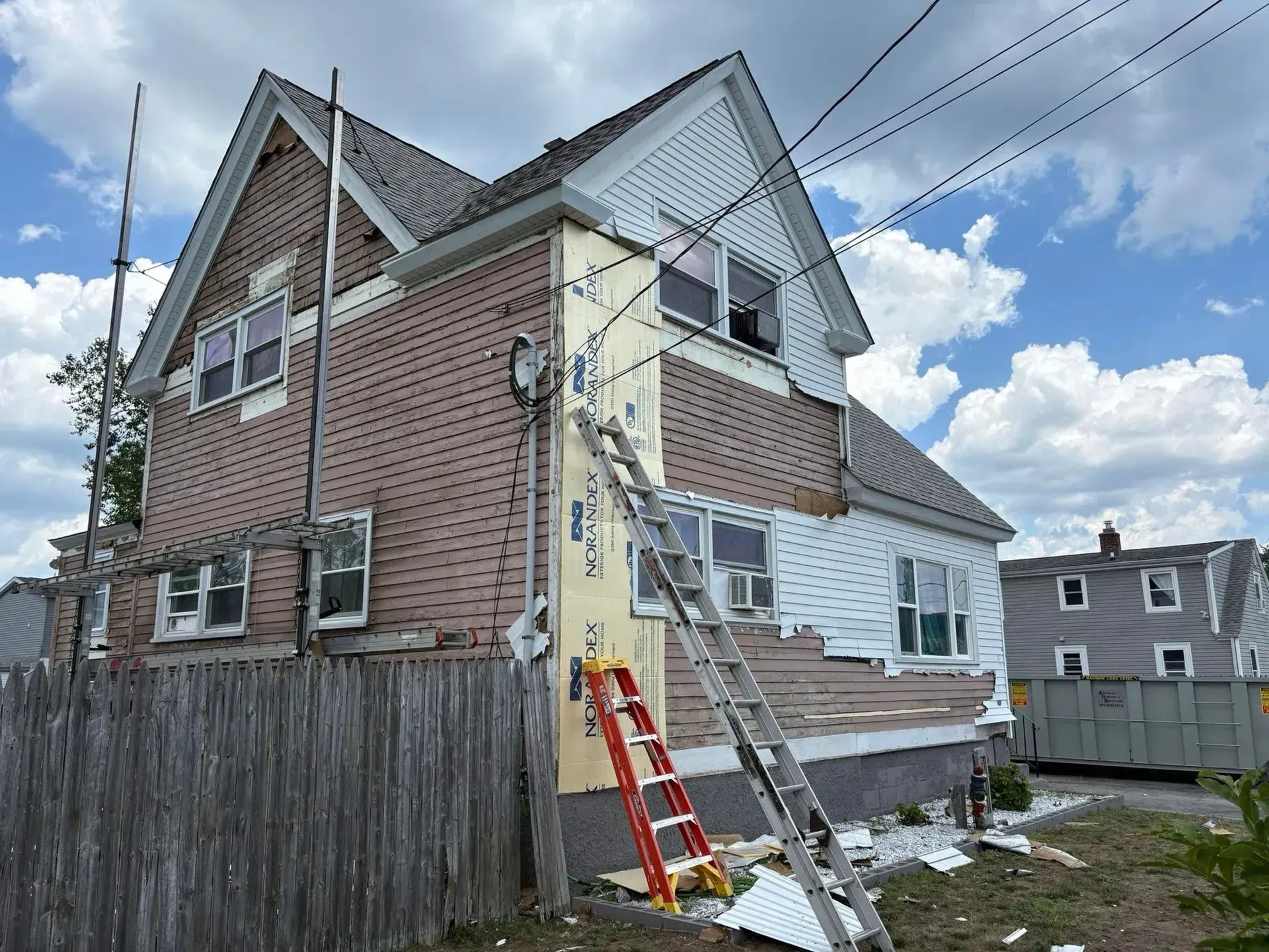 Two-story brick house with a ladder leaning against it and an extension ladder on the side wall.