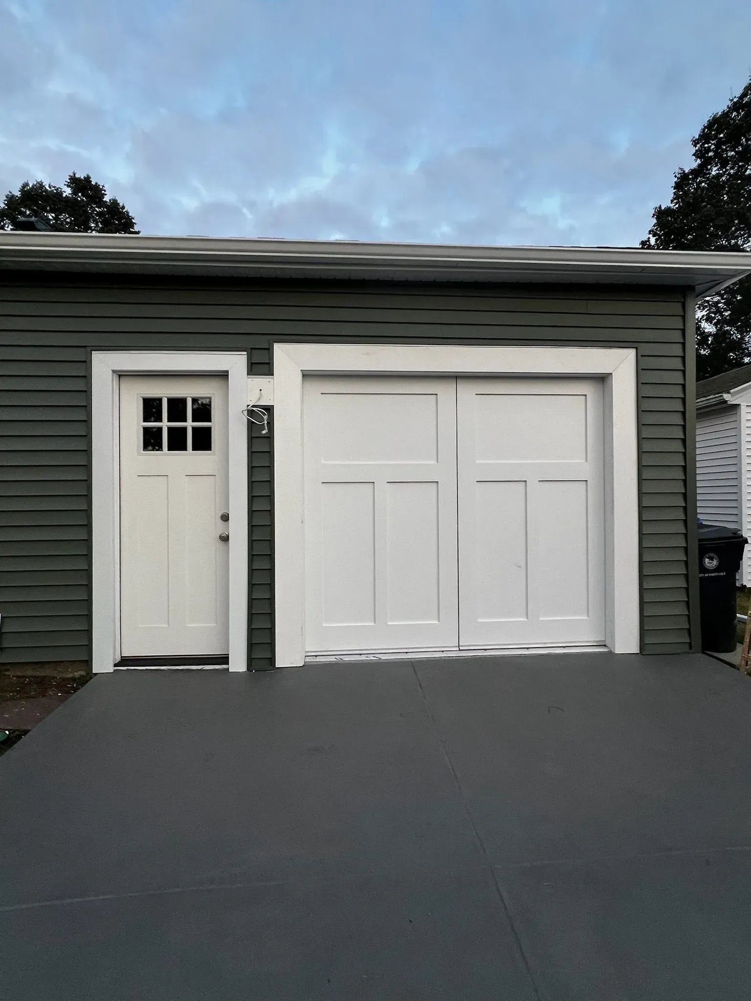White garage and side entry door on gray house with dark driveway at dusk