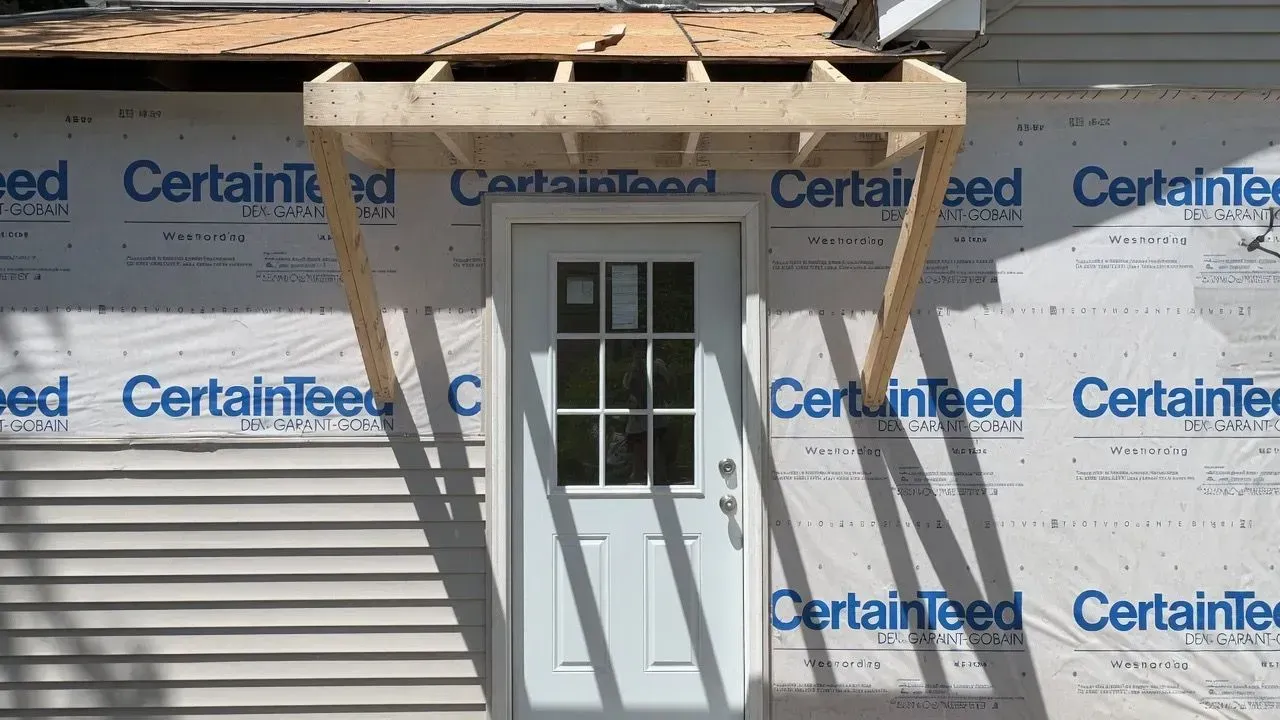 House exterior under construction with white siding, exposed roof, and a white door with windows