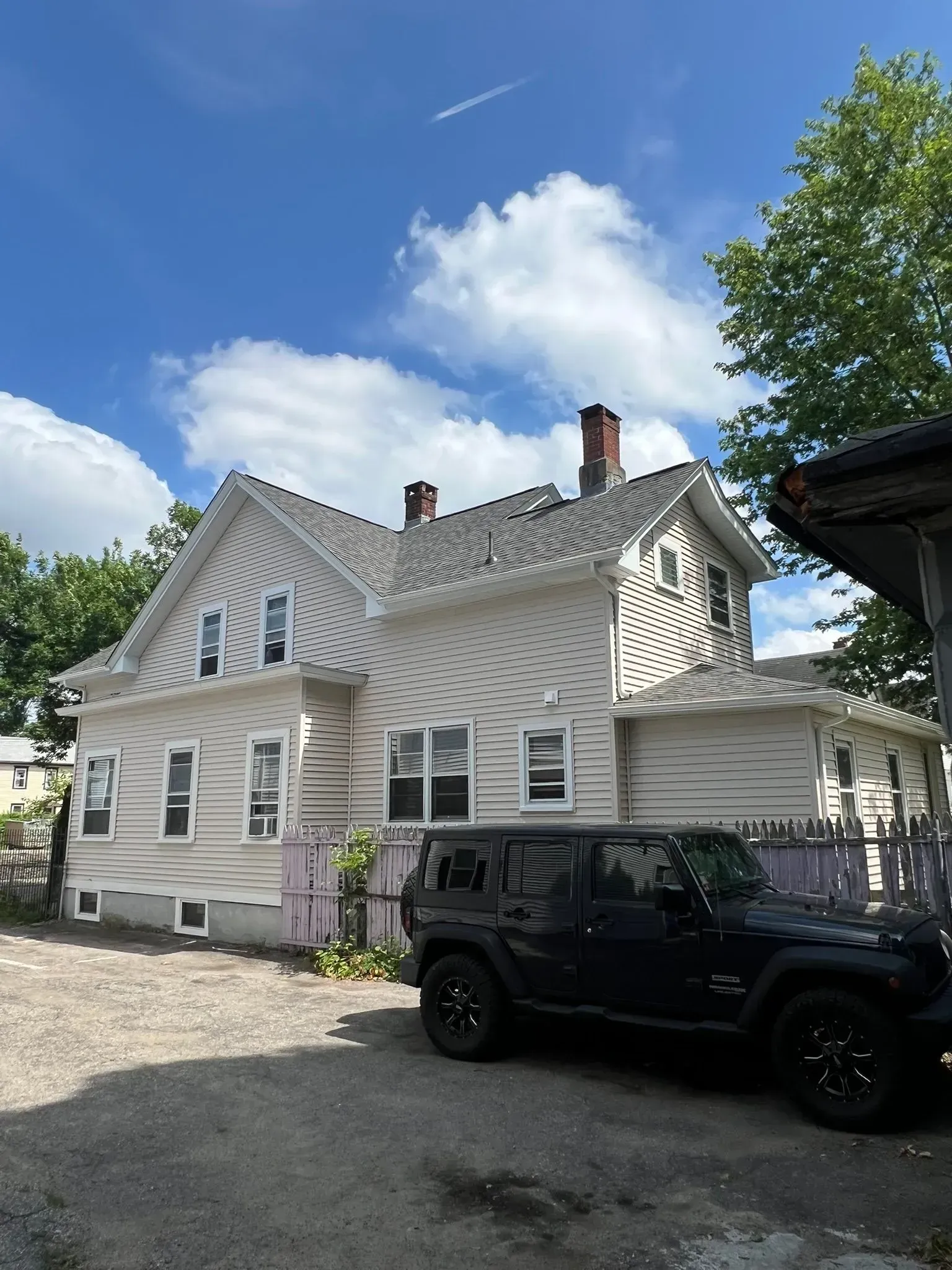 White two-story house with gray trim and a black SUV parked in the driveway under a blue sky.