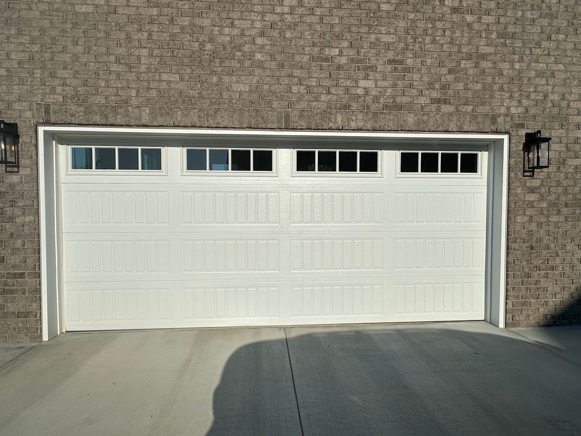 White garage door with windows, brick wall background, two lights on sides.