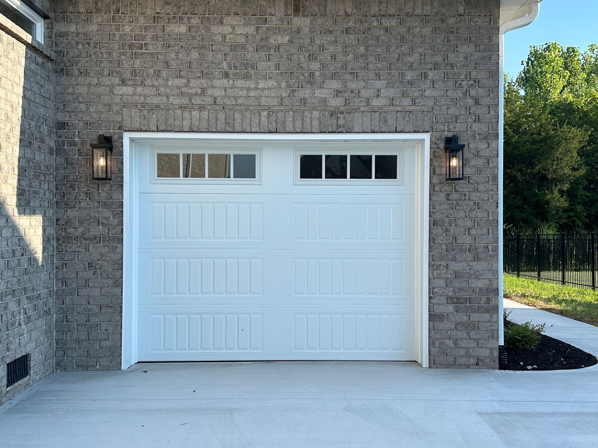 White garage door with windows, flanked by brick and sconce lights. Concrete driveway.