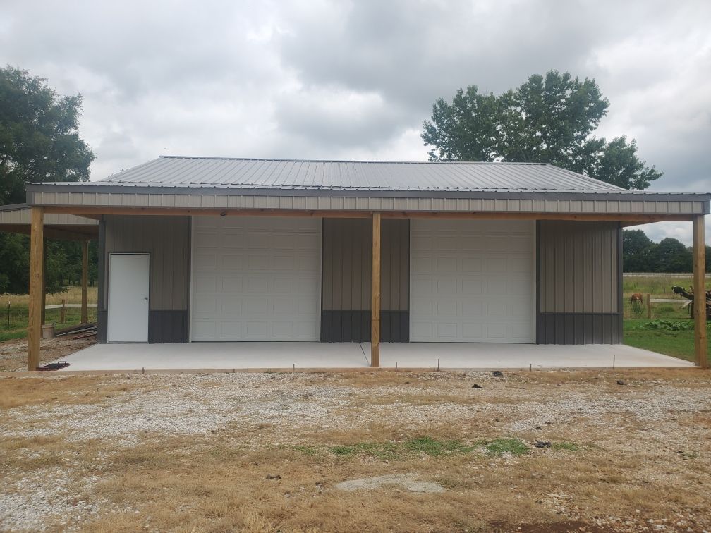 Tan and gray metal garage with two doors under a covered porch; gravel driveway in front.