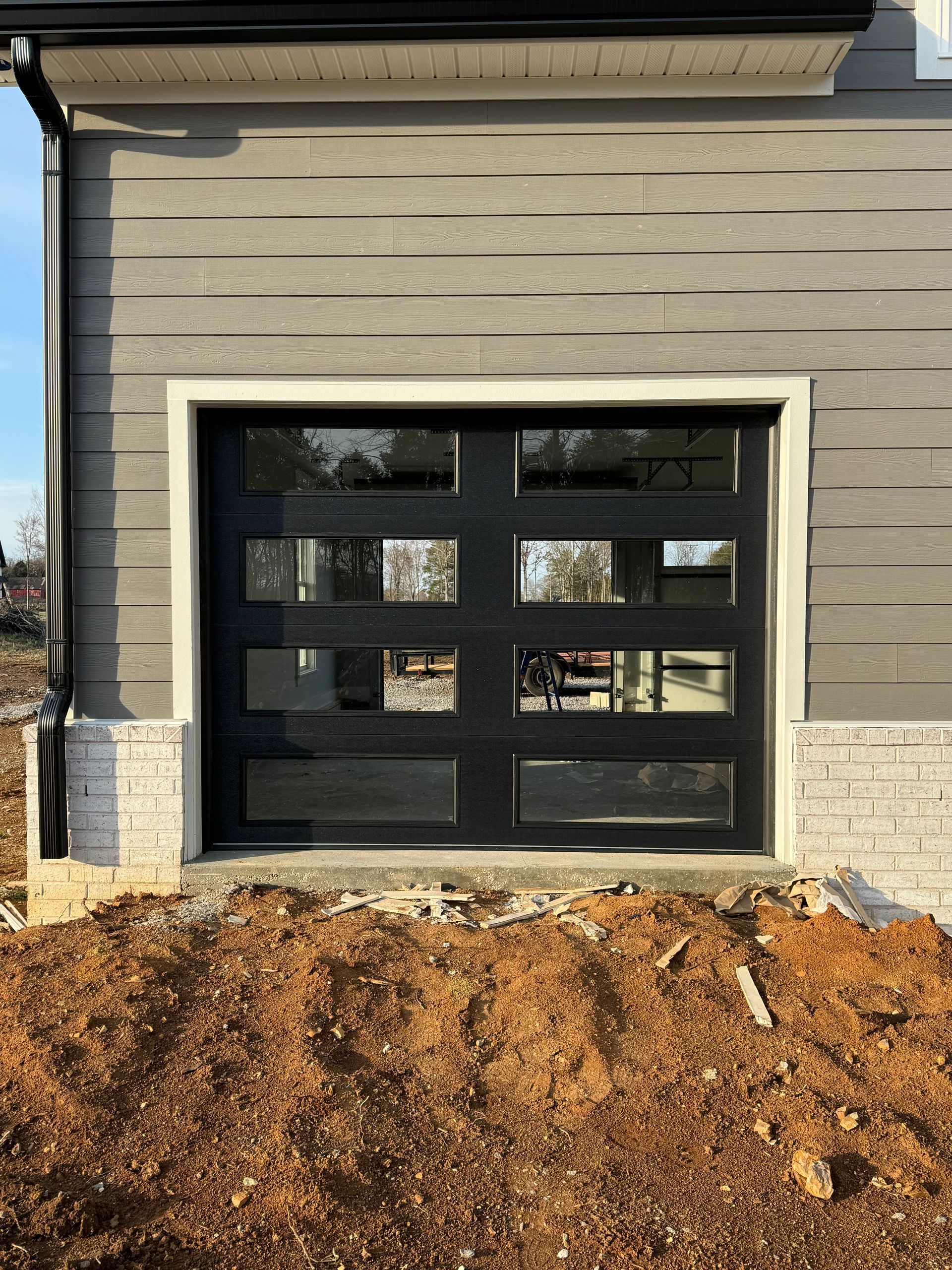 Black garage door with multiple glass panels, white trim, and light gray siding.