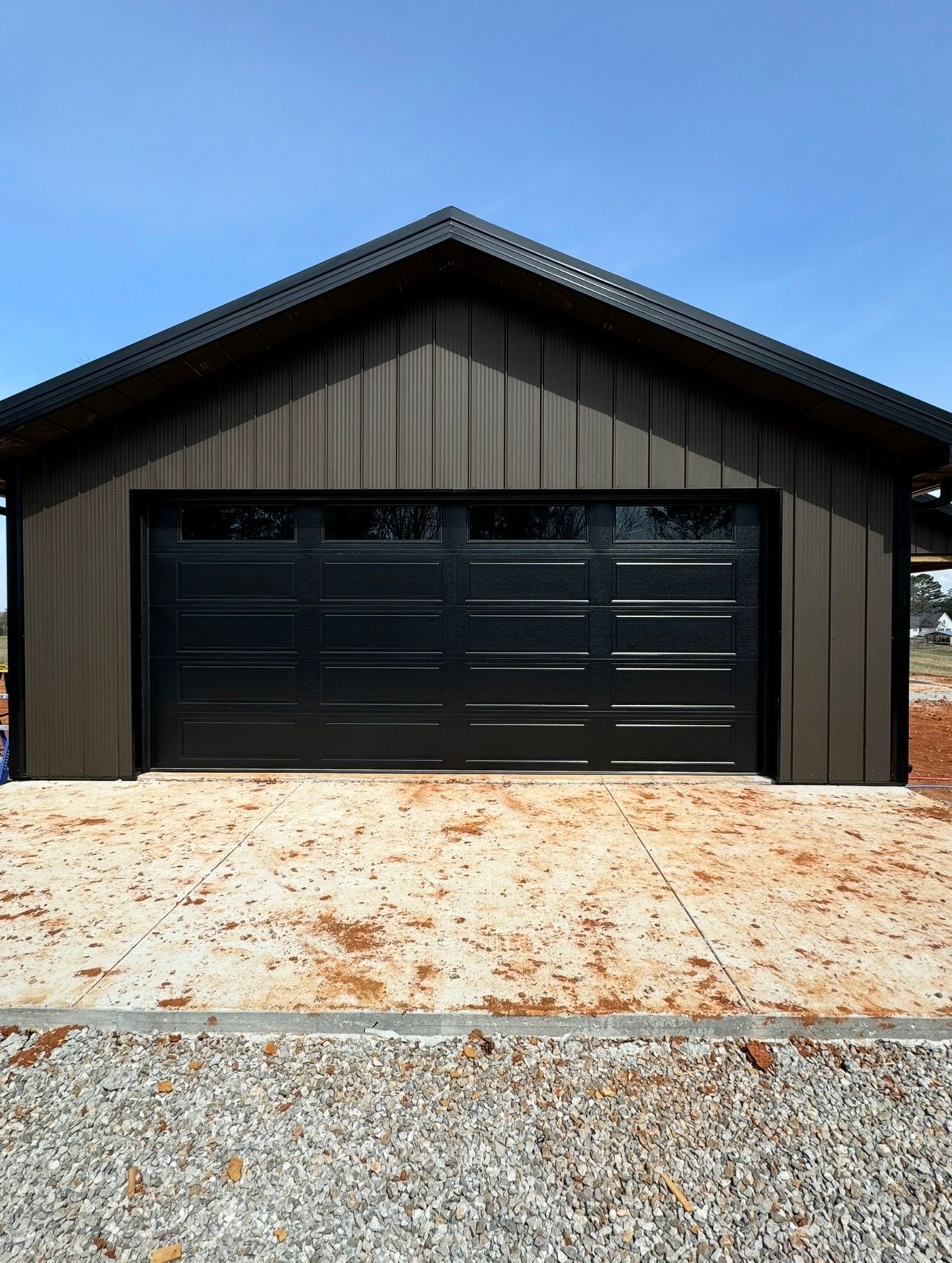 Dark brown metal-clad garage with black door, windows, and roof against a clear blue sky.