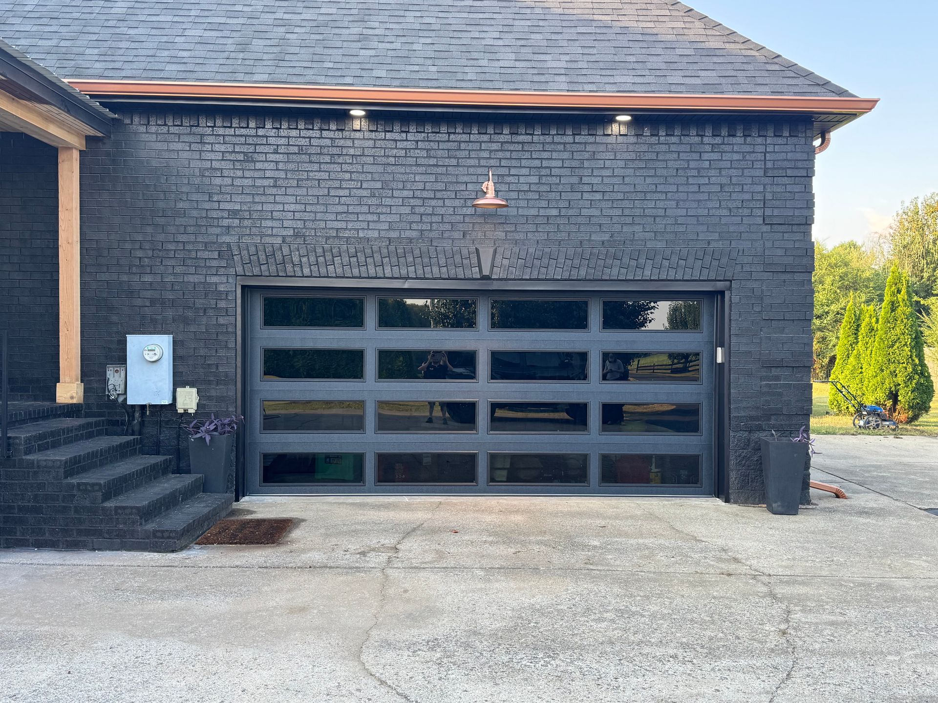 Black painted brick garage with a modern glass door, copper guttering, and concrete driveway.