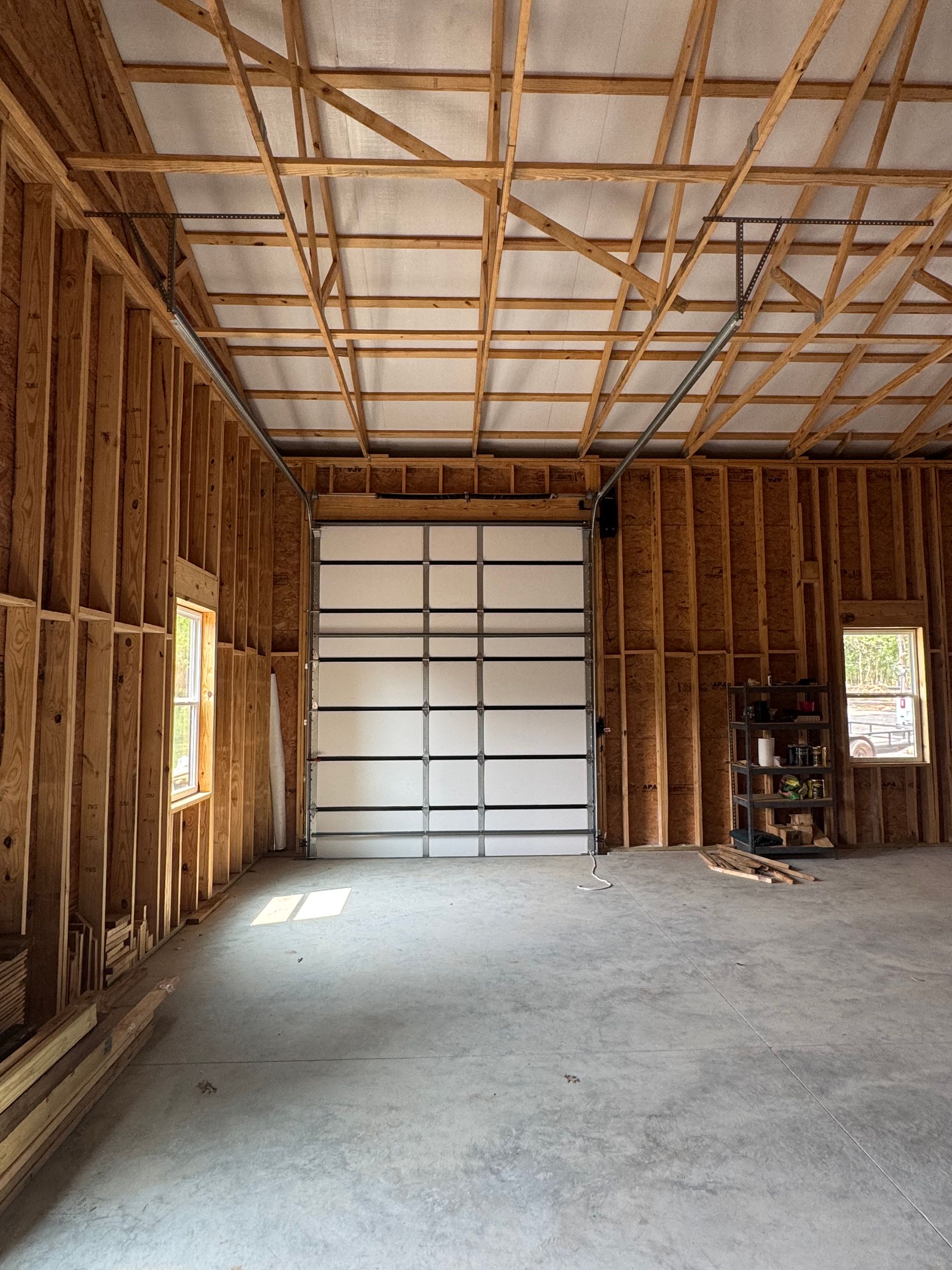 Interior of a new, unfinished garage with a closed overhead door and bare wooden walls.