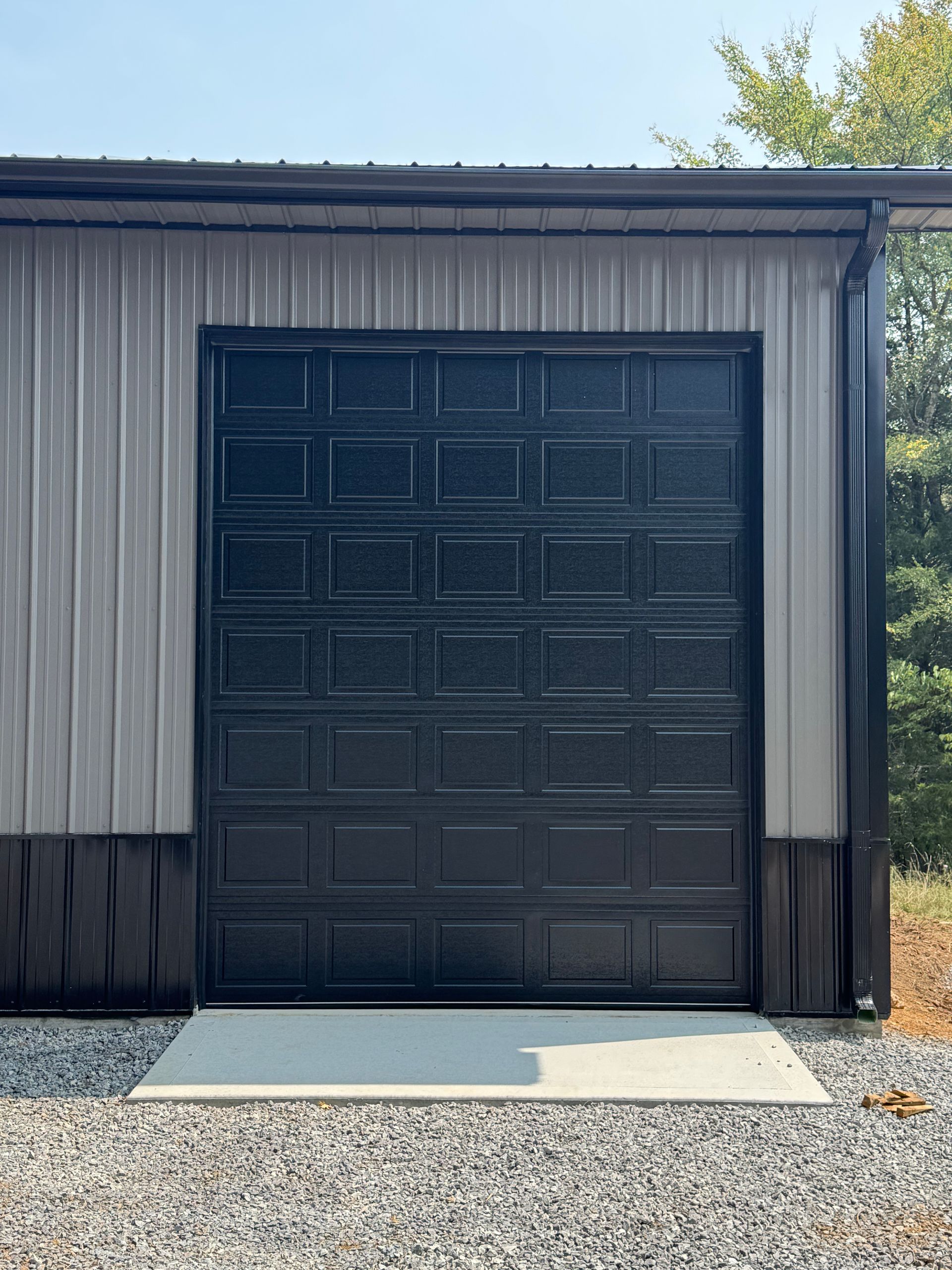 Black garage door in a gray and black metal building with a concrete slab entrance.