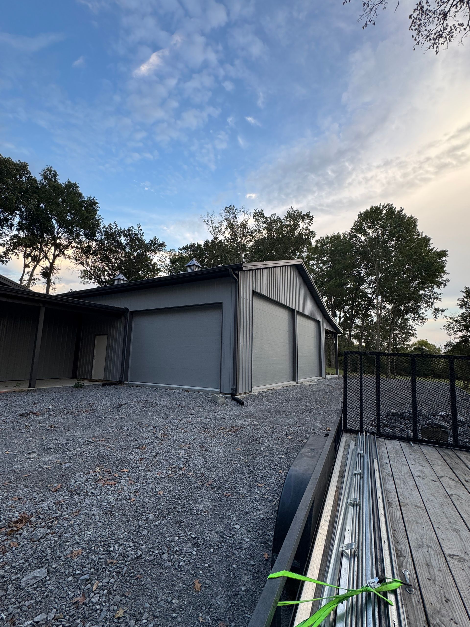 Gray garage with two doors on a gravel driveway, with a blue sky.