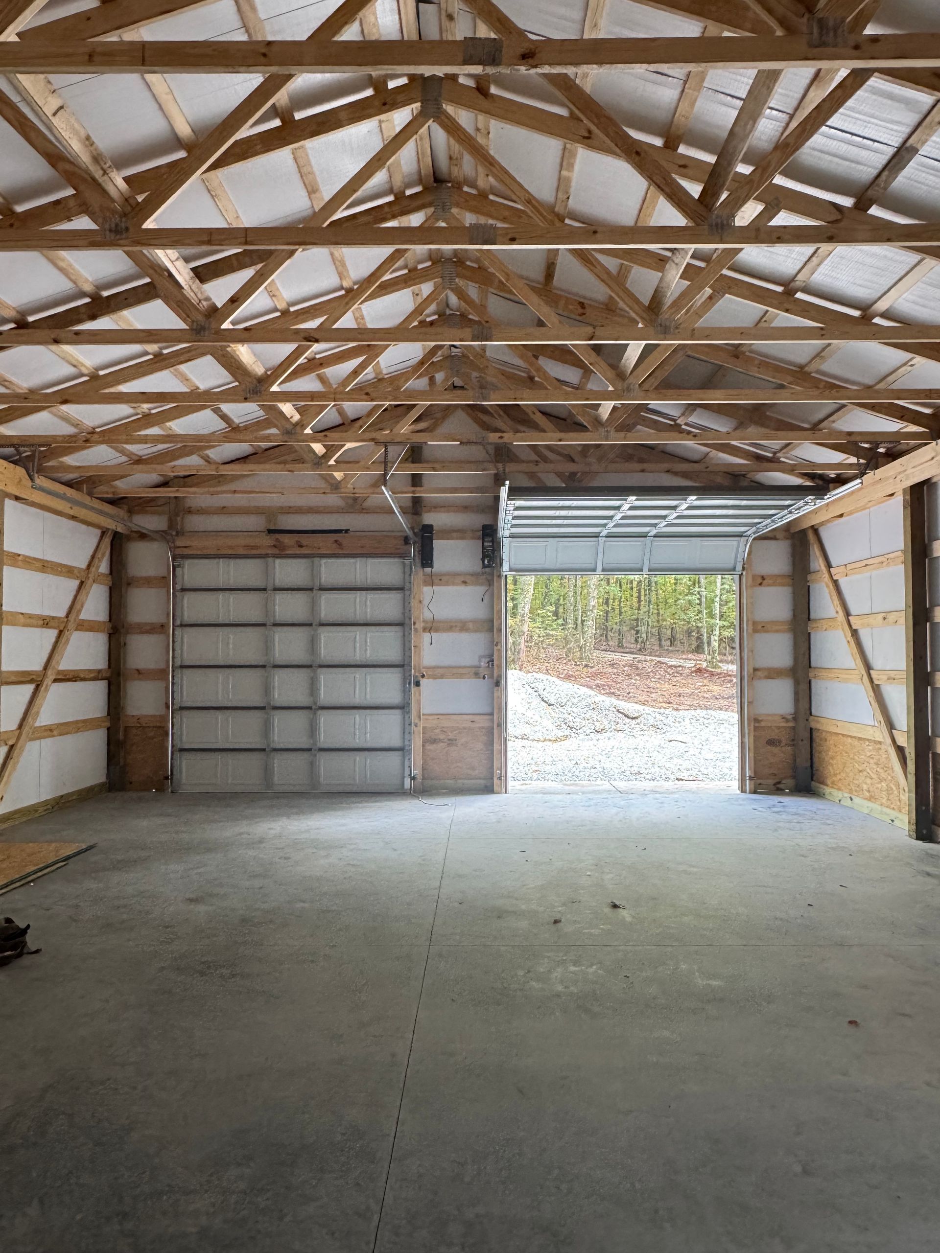 Interior of a large unfinished garage with a concrete floor, two garage doors, and wooden beams.