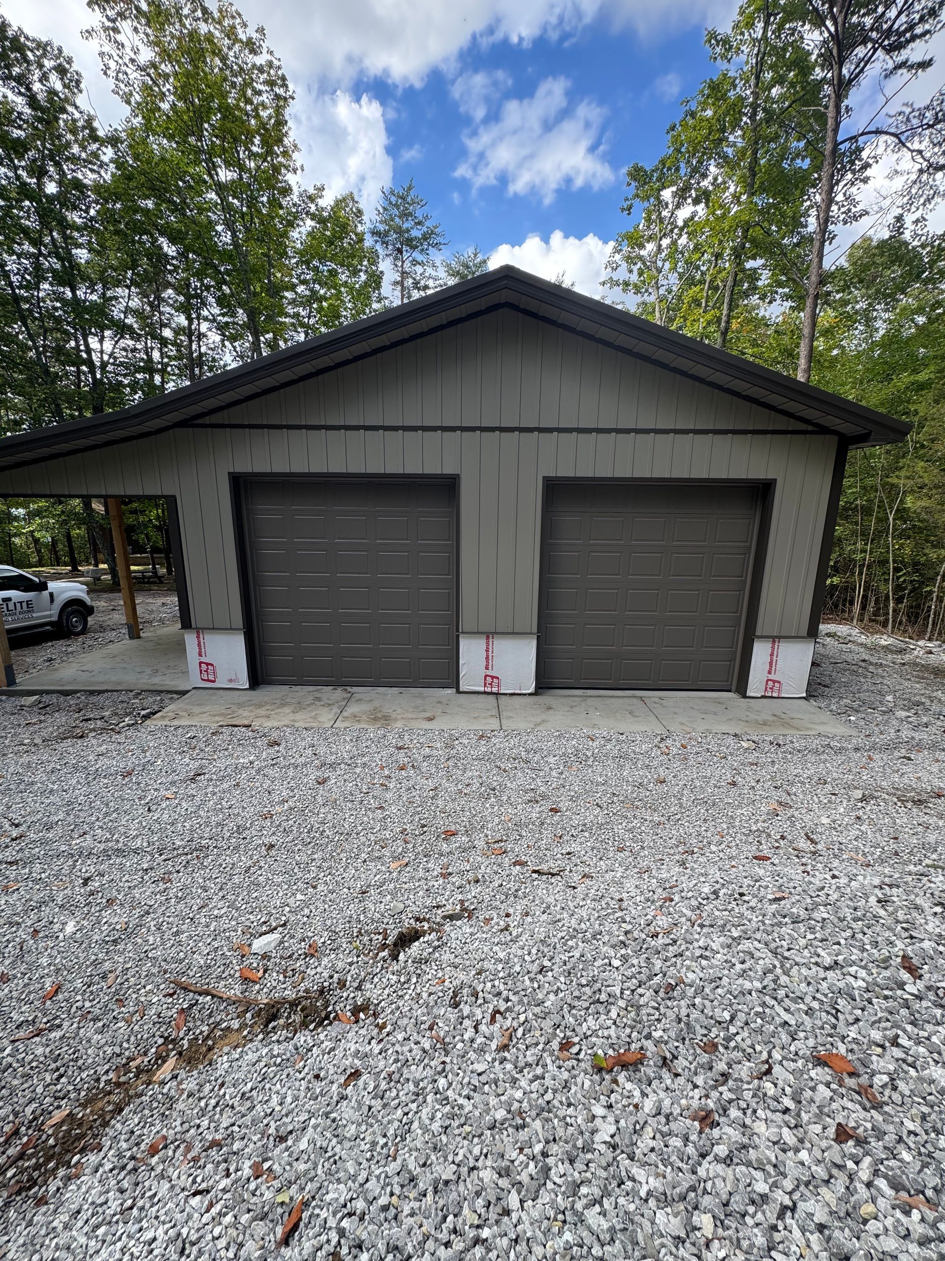 Two-bay garage with brown doors, gray siding, and a gravel driveway.