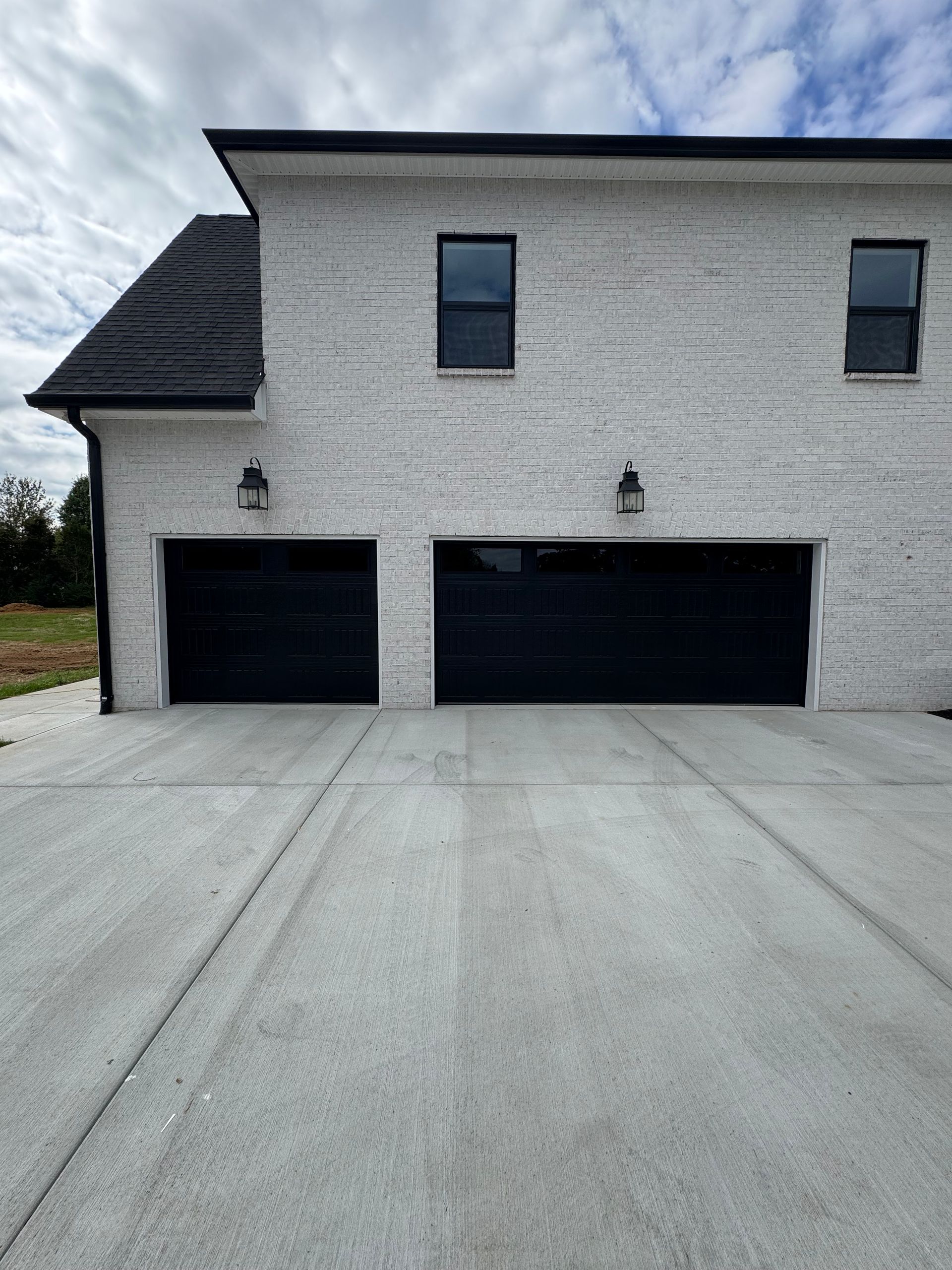 White brick house with two black garage doors, two windows, and a concrete driveway.