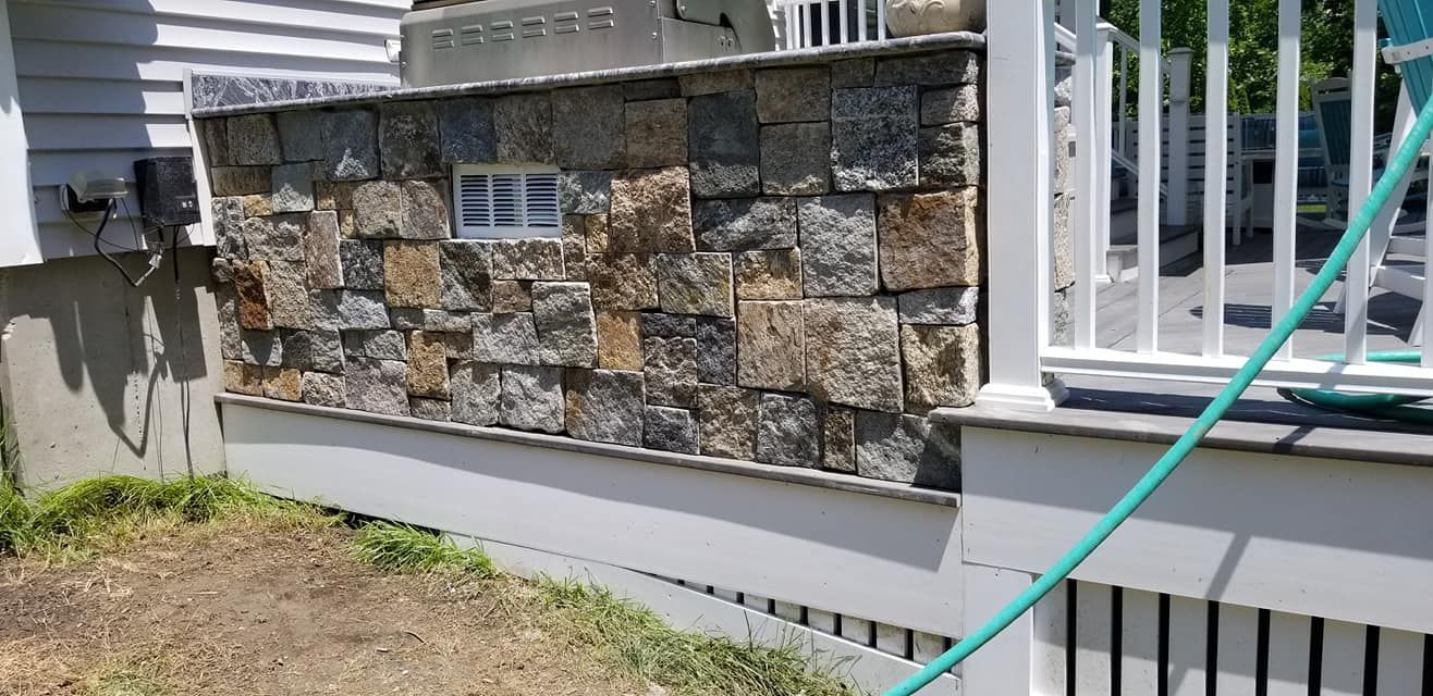 Stone wall with a small window, next to a white deck with a railing.