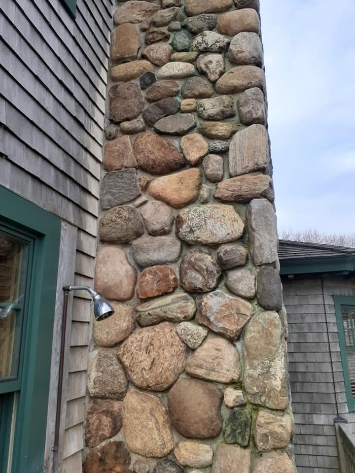 Stone chimney on the exterior of a shingled building; outdoor shower visible.