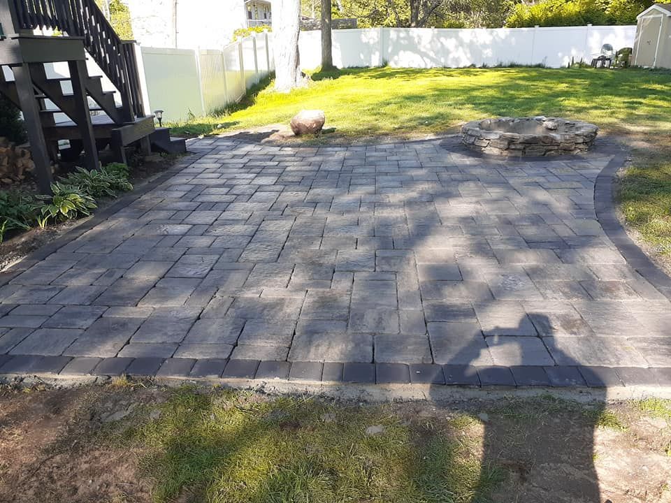 Brick patio in a backyard, with a fire pit and bordering dark bricks.