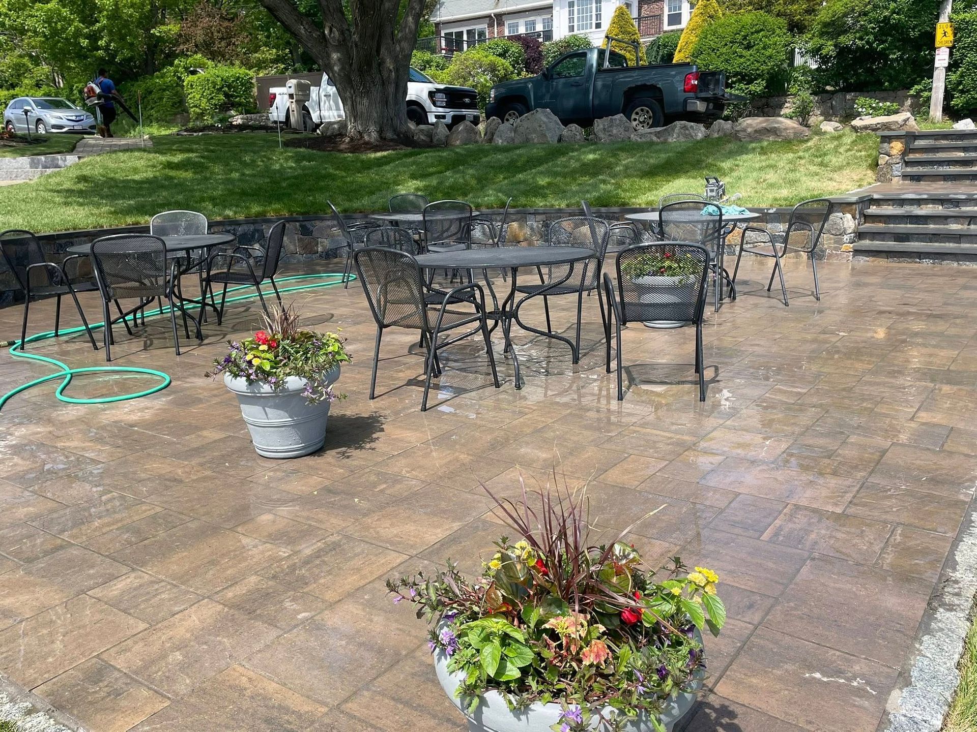 Patio with tables and chairs being washed; flower pots with colorful flowers on the patio.