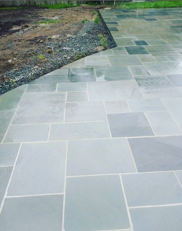 Blue-gray stone patio with various sized rectangular pavers next to dirt and gravel.