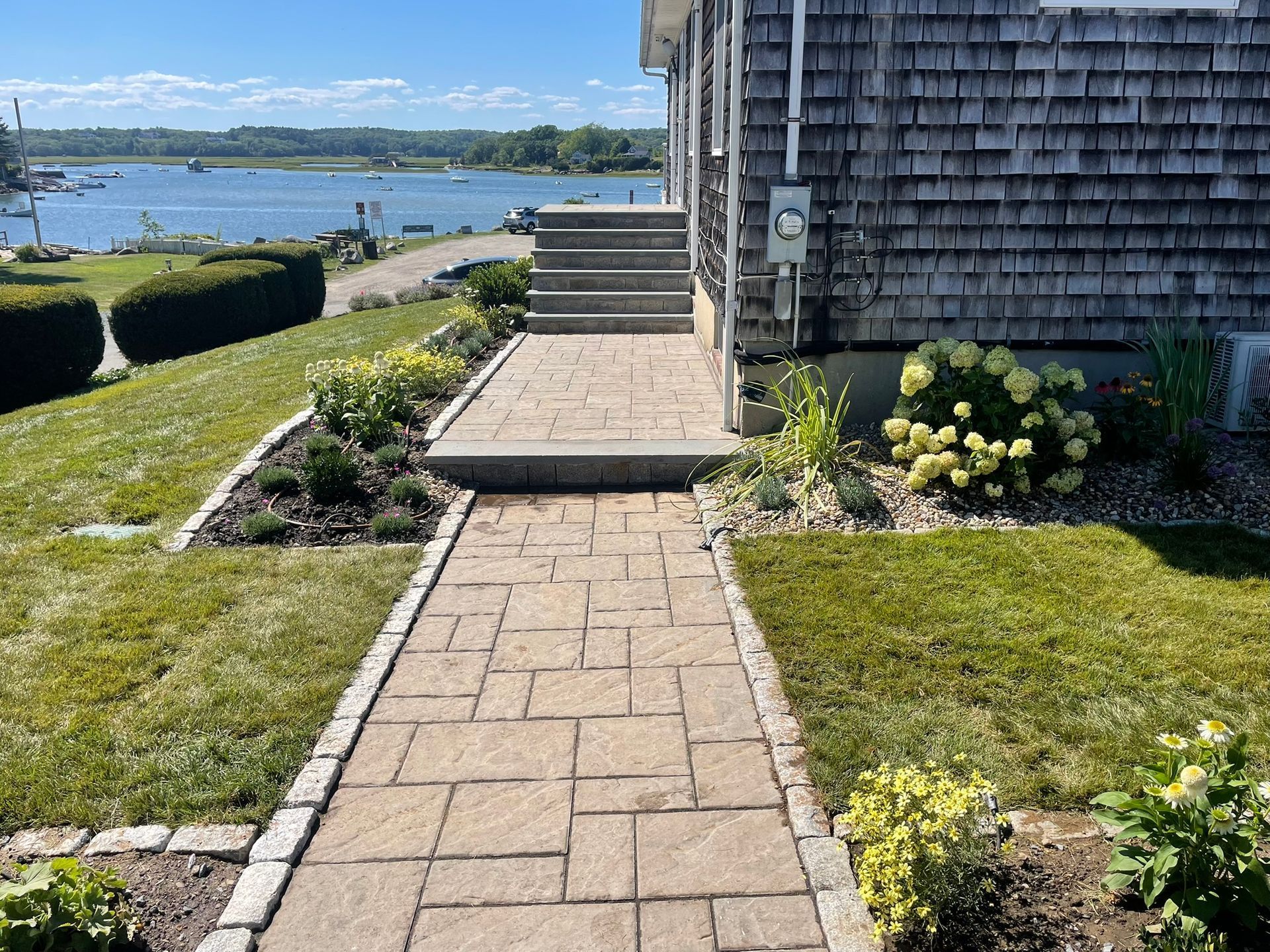 Person wearing yellow gloves laying paving stones on a sandy surface, with a hammer and measuring tape nearby.