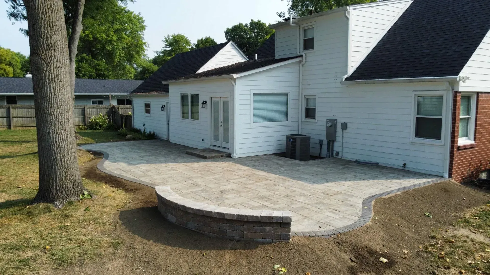 Backyard patio with curved stone edging beside a white house and garage.