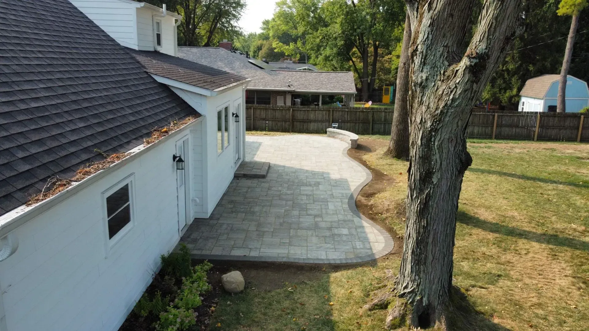 White house exterior with curved concrete patio and large tree in a grassy yard
