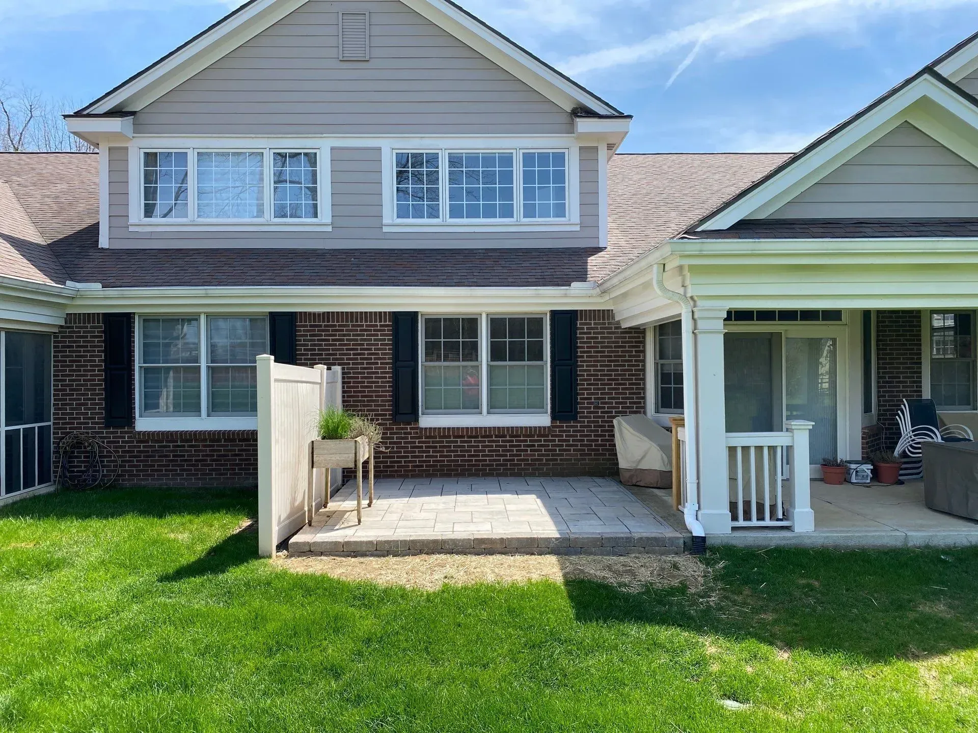 Front view of a townhouse with brick and vinyl siding, a covered patio, and green lawn
