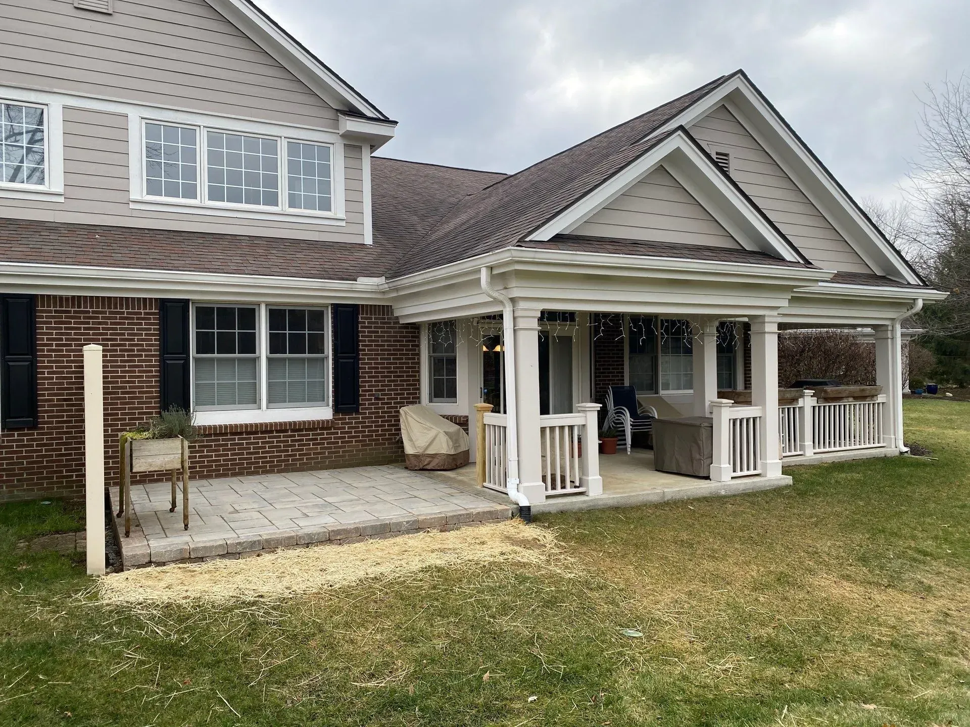 Brick house exterior with covered porch, white railings, and a stone patio in front of a lawn