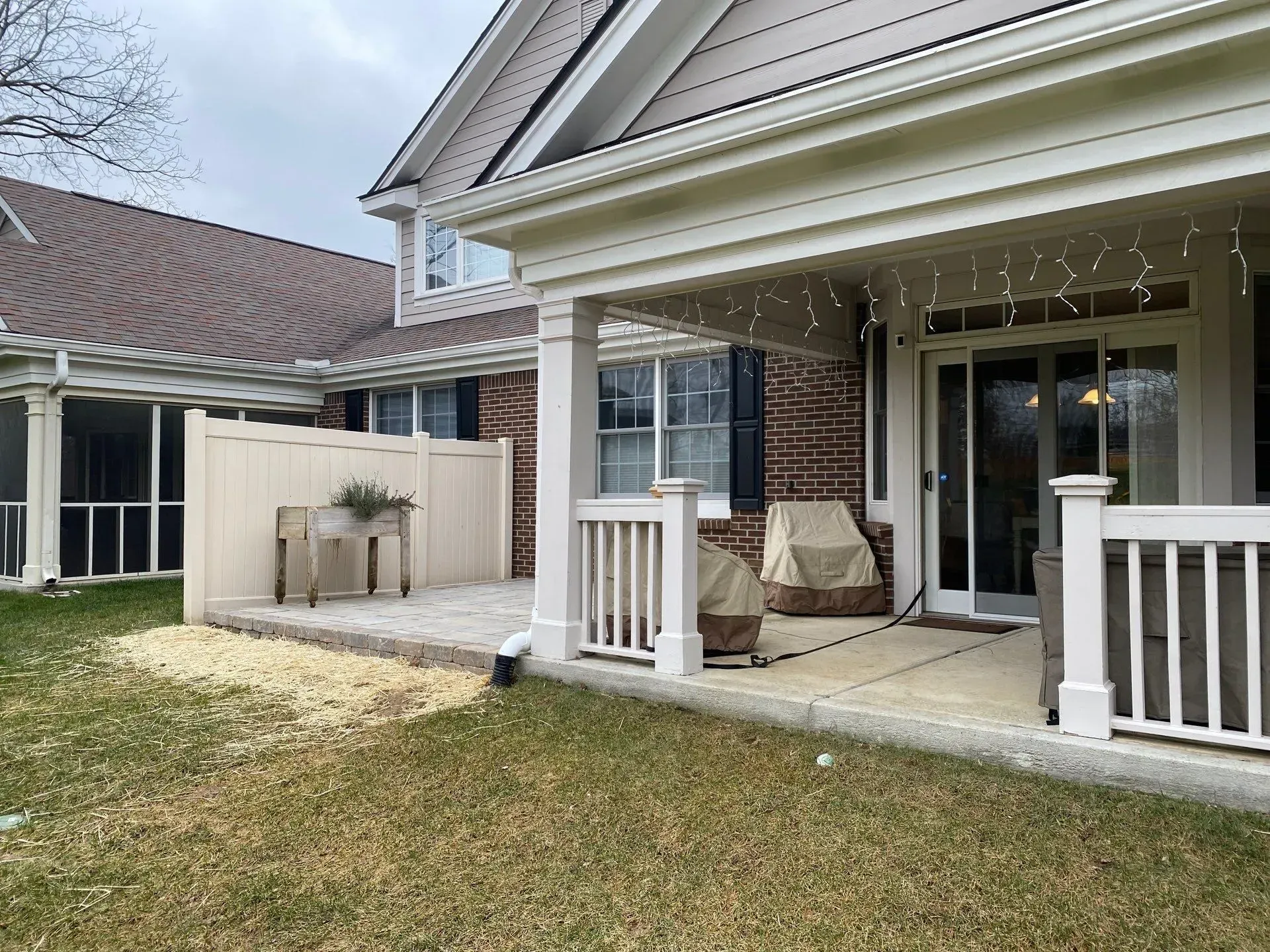 Covered backyard patio with white railings, string lights, seating, and a small outdoor sink area.