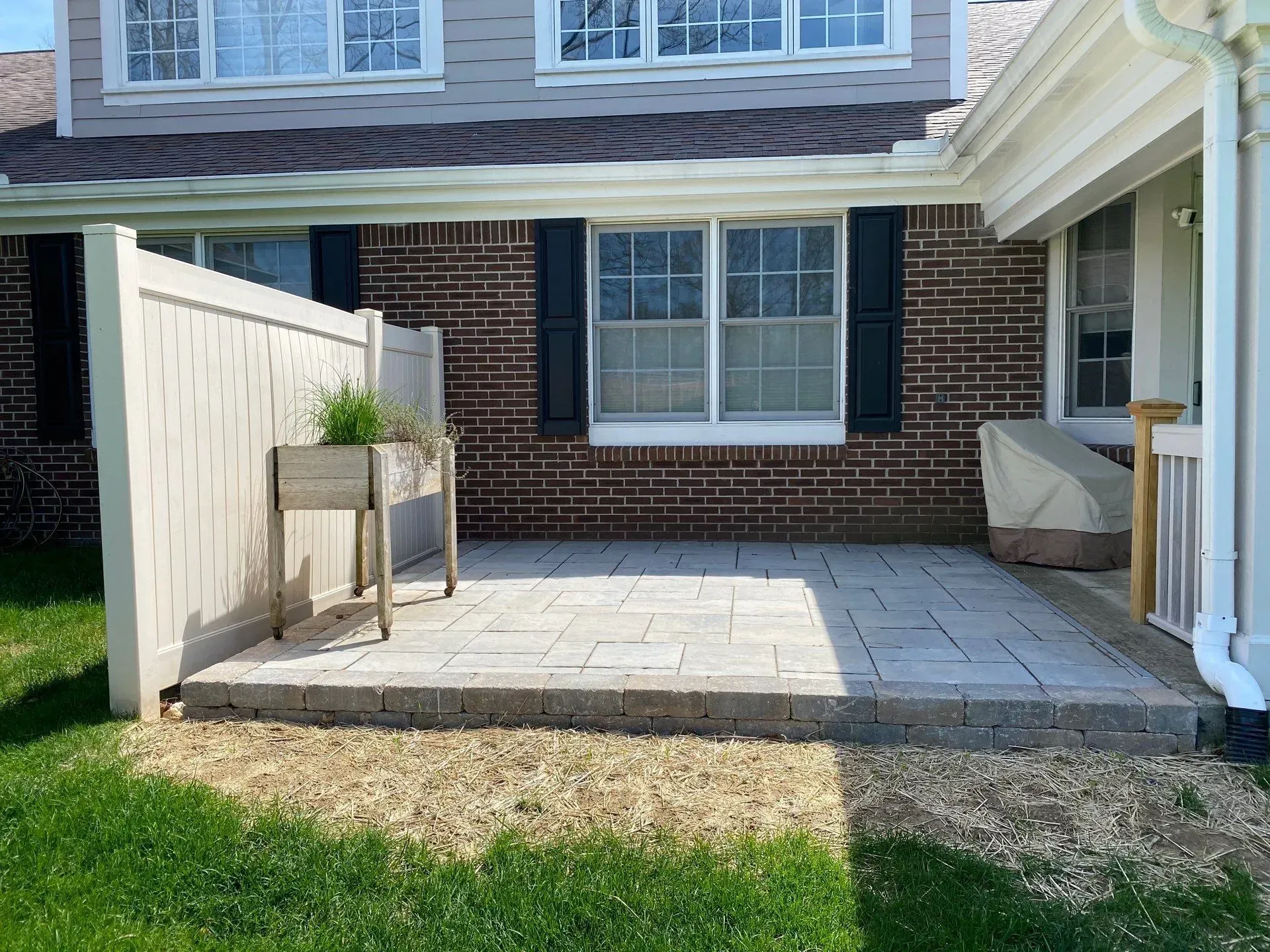 Patio with stone pavers, brick wall, white fence, and potted plant beside a house