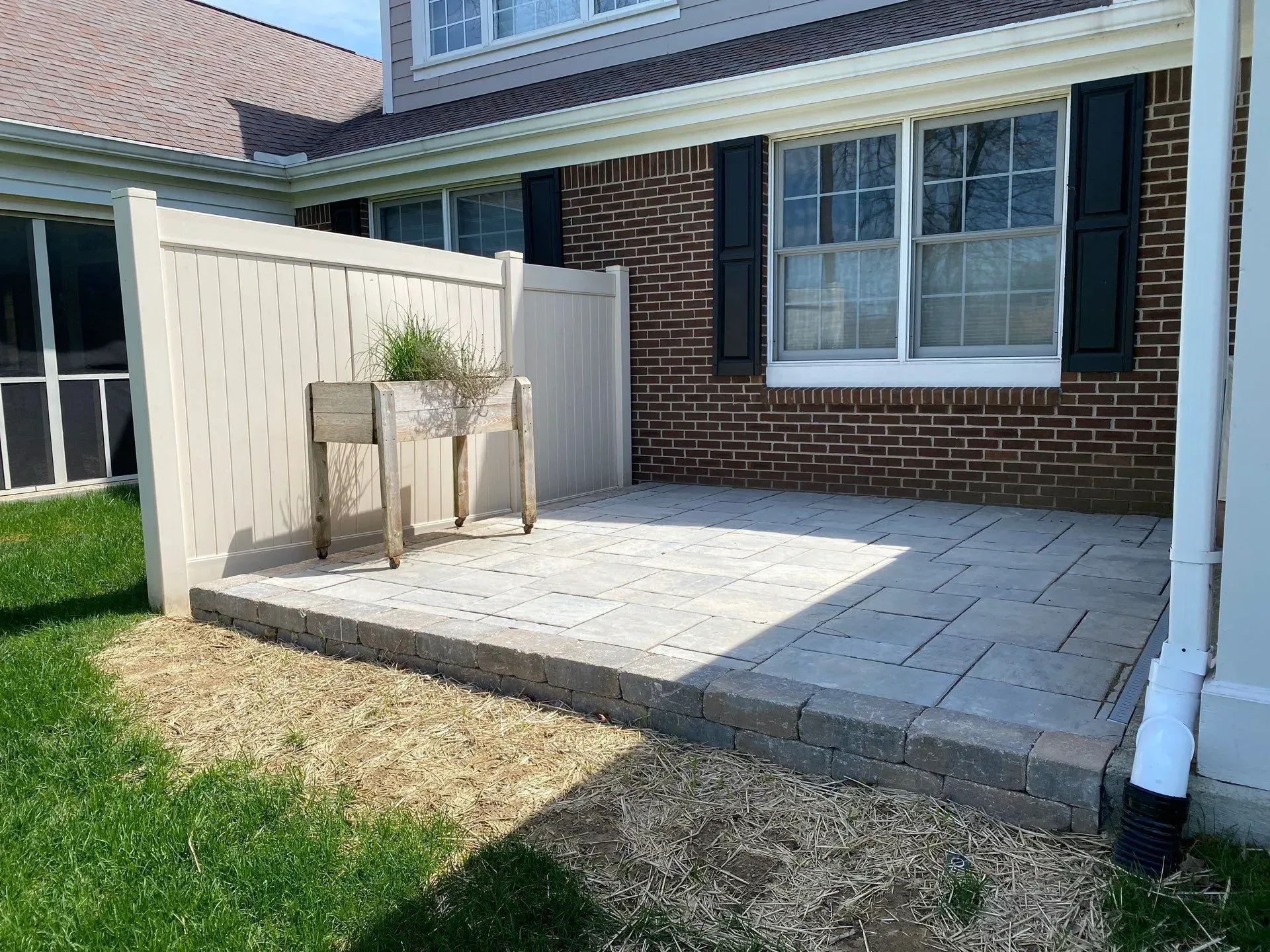 Backyard patio with stone pavers, brick wall, potted plant, and covered seating area
