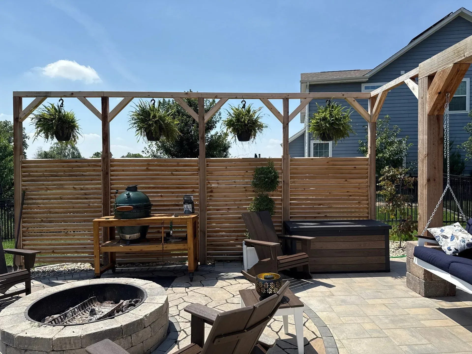 Backyard patio with fire pit, wooden bench, planters, and lounge chairs in bright sunlight