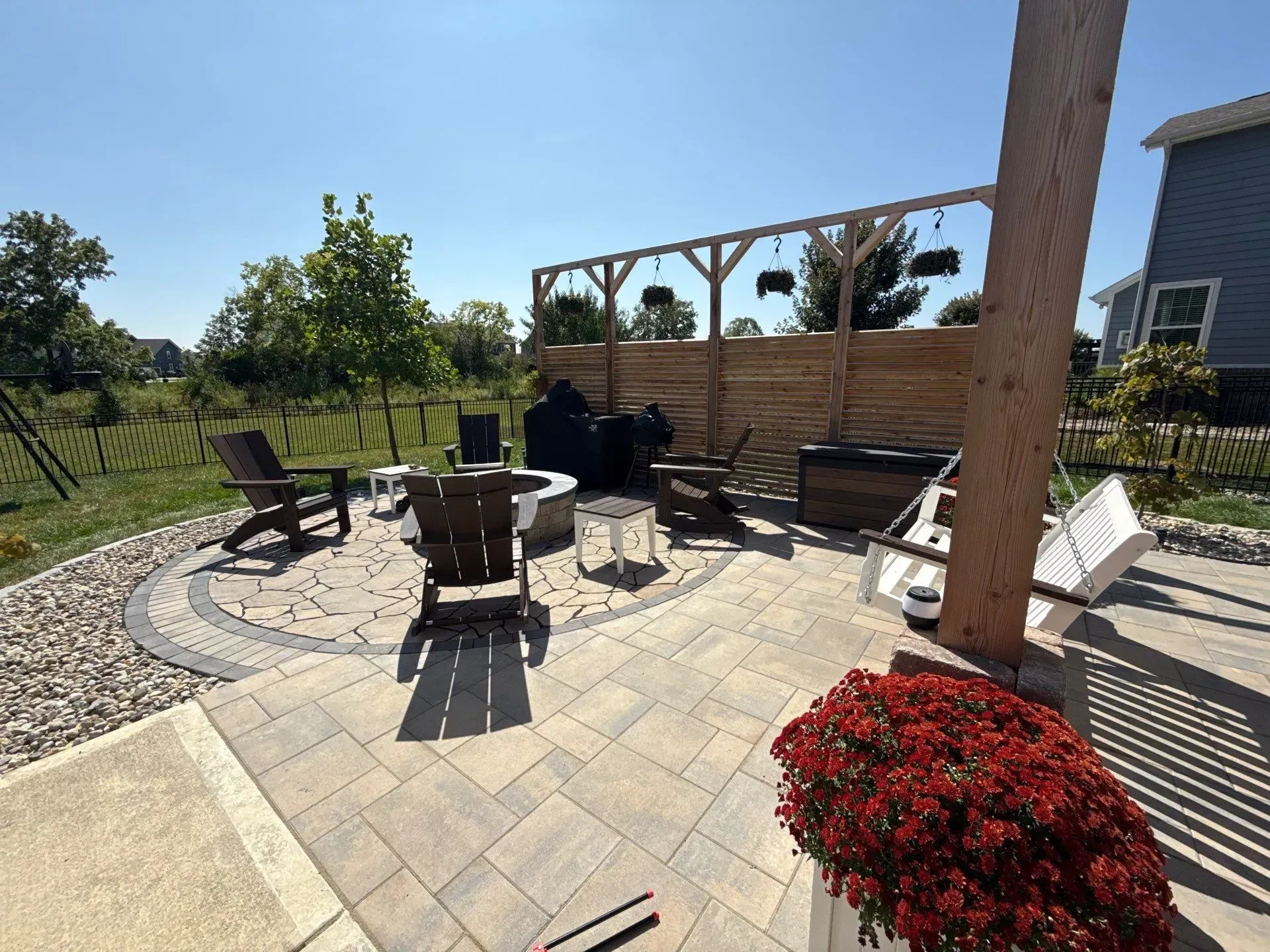 Backyard patio with stone pavers, fire pit seating, pergola, and red flowers in the foreground