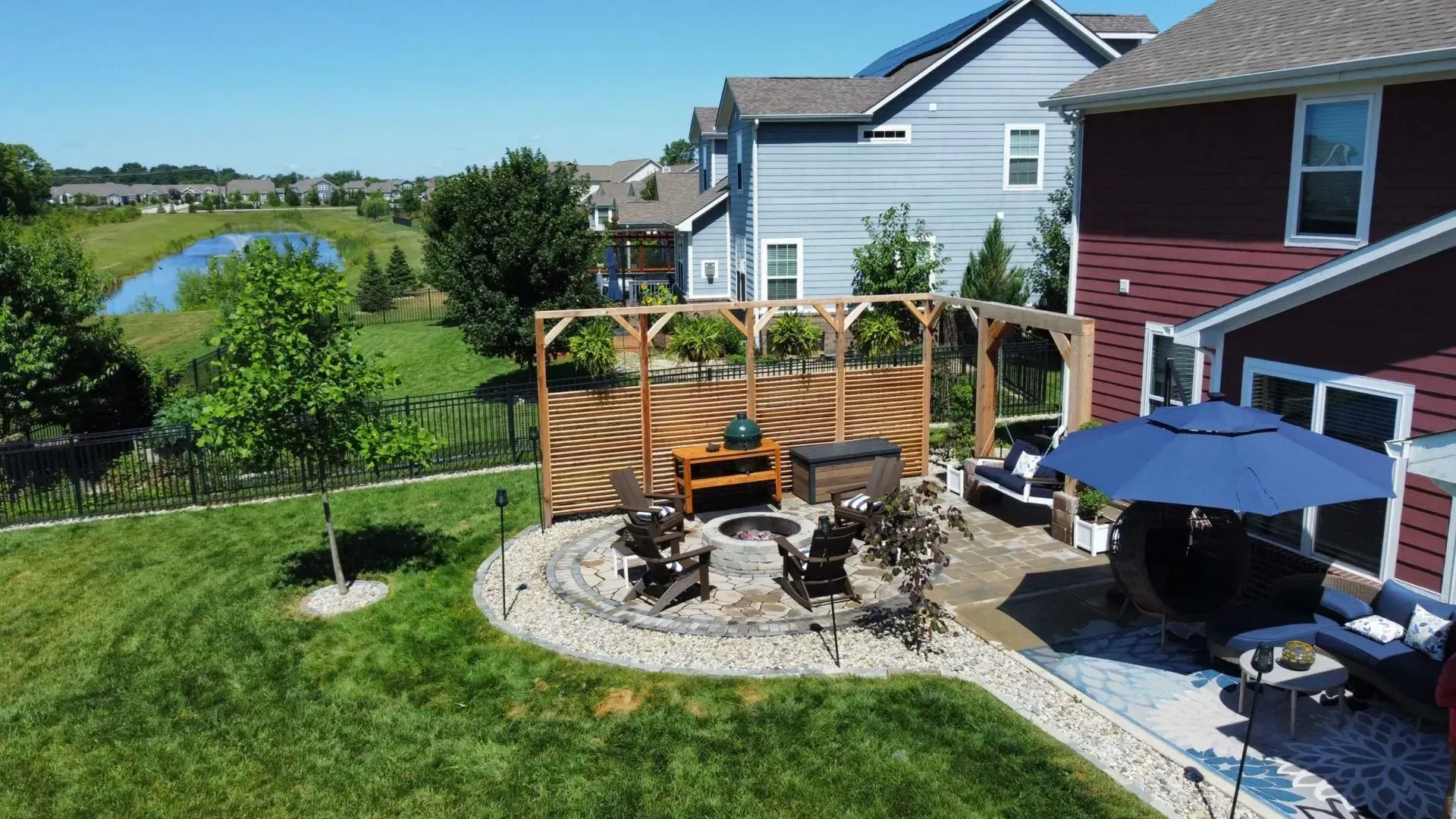 Backyard patio with fire pit, umbrella table, wooden fence, and river view beside two houses