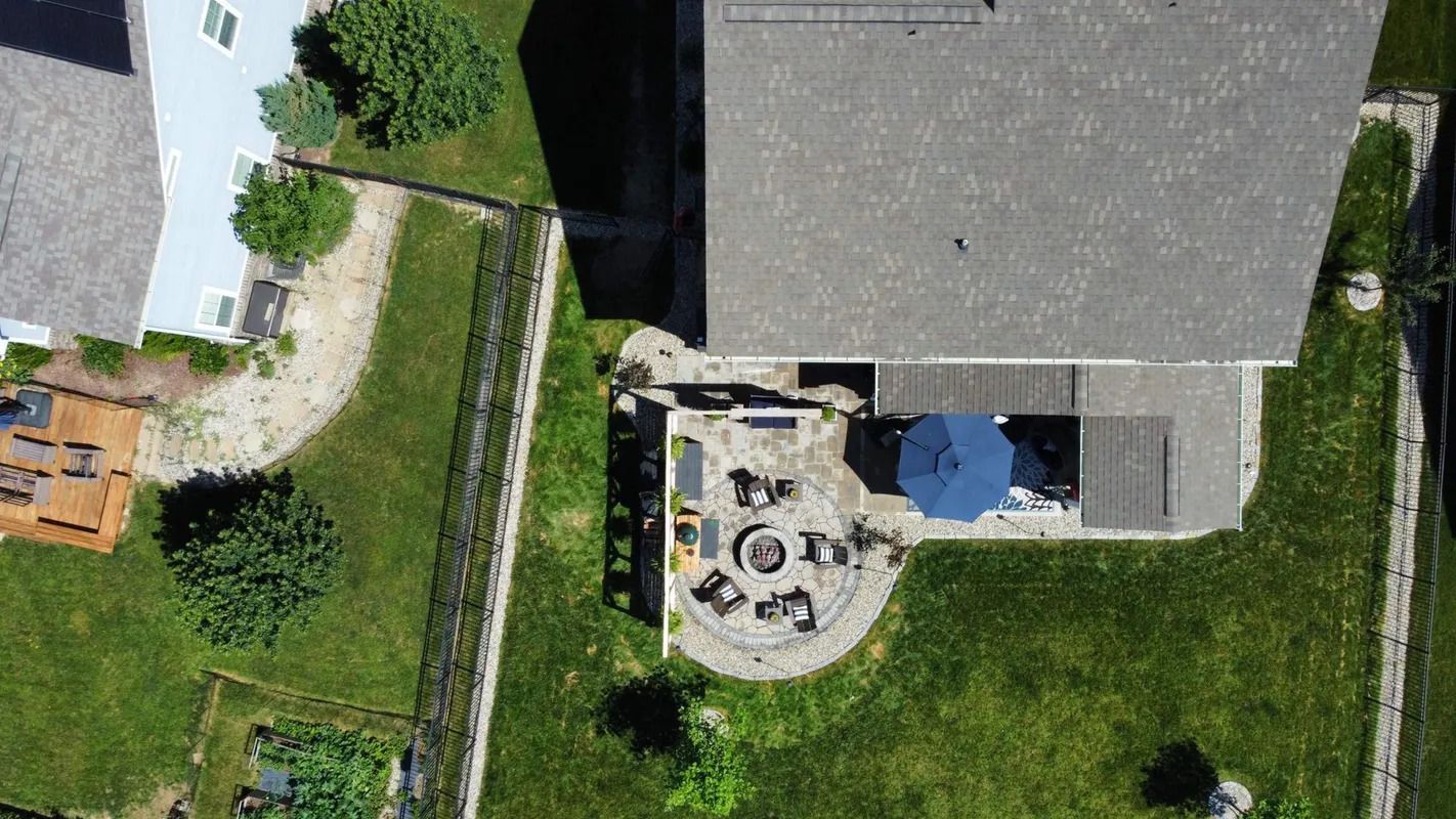 Aerial view of a backyard patio beside a house, with outdoor furniture and a blue umbrella.