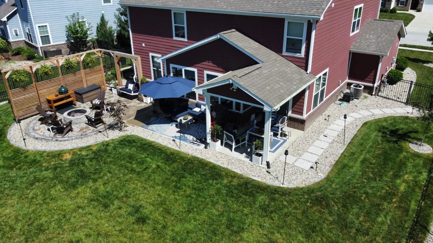 Aerial view of a red house with a covered patio, stone walkway, and green lawn.