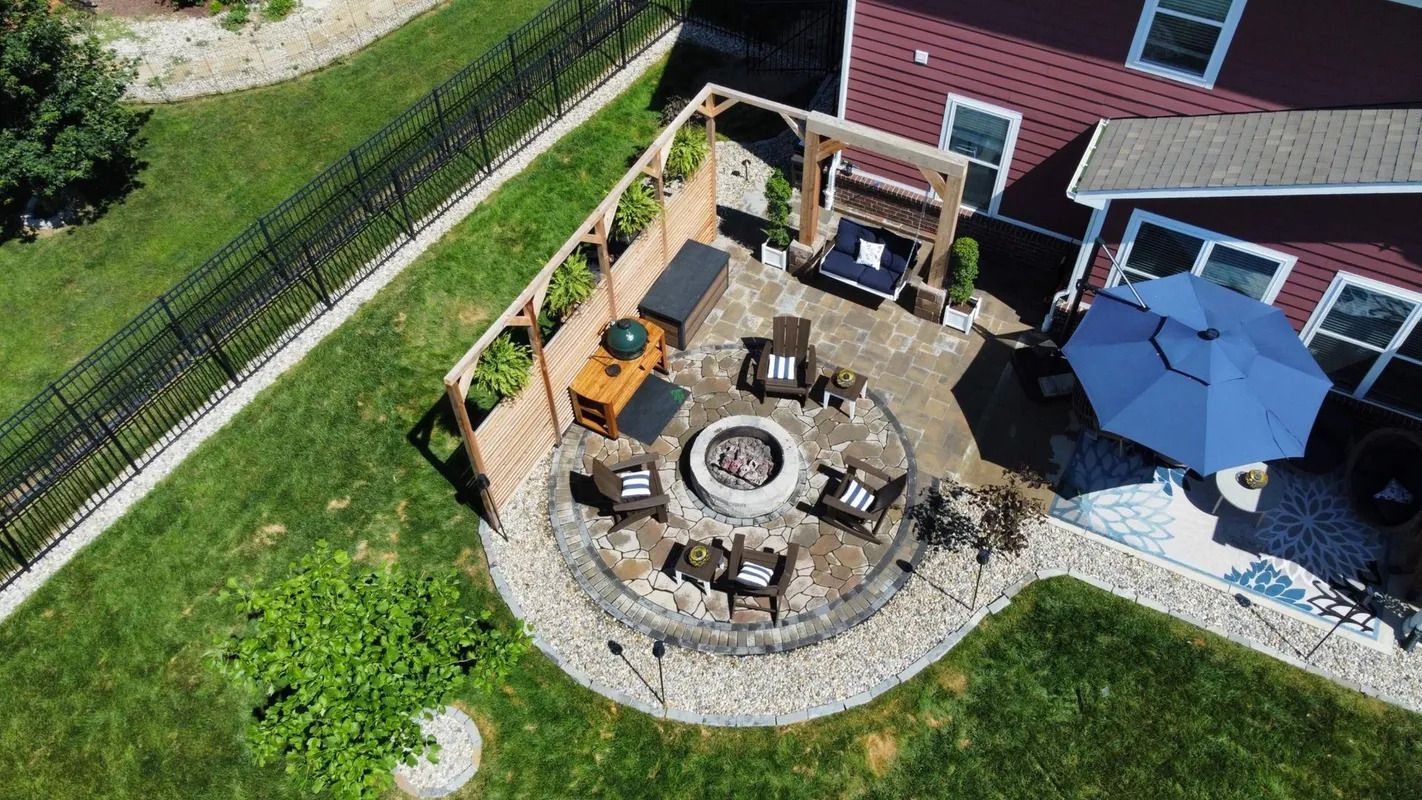 Aerial view of a backyard patio with a fire pit, chairs, blue umbrella, and a toy excavator near a house
