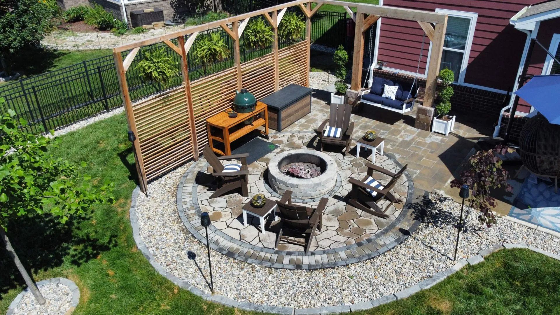 Backyard patio with a fire pit, chairs, grill, and wooden pergola on a gravel border