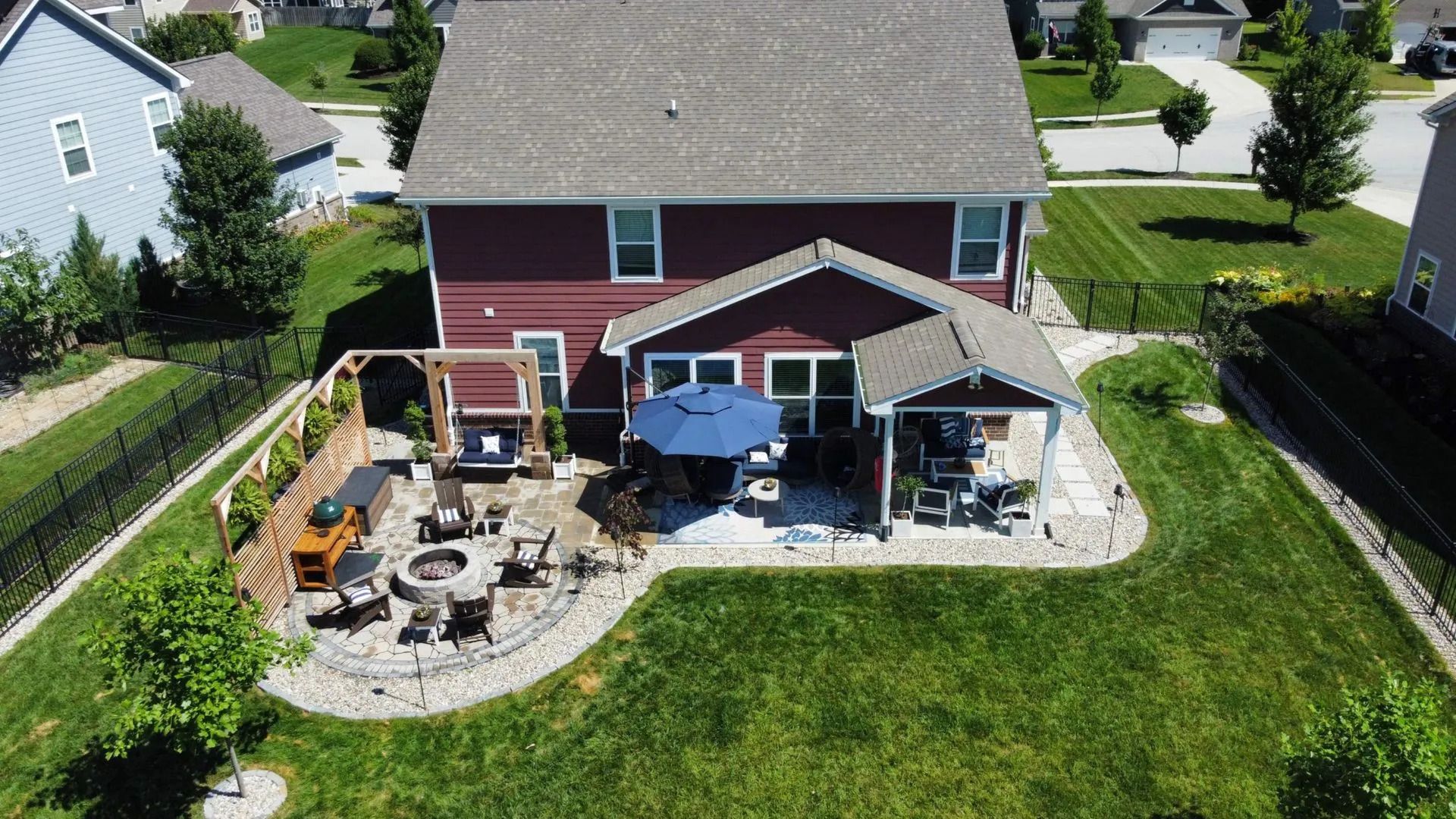 Backyard patio with fire pit, umbrella, seating, and grill behind a red two-story house