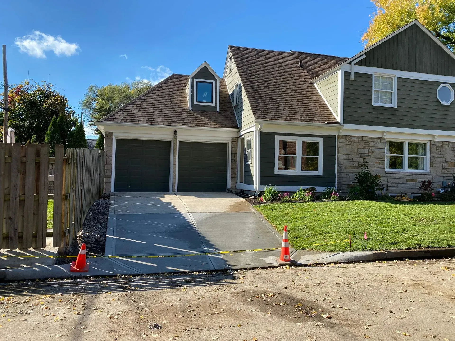 House with double garage and newly poured concrete driveway marked by orange cones.
